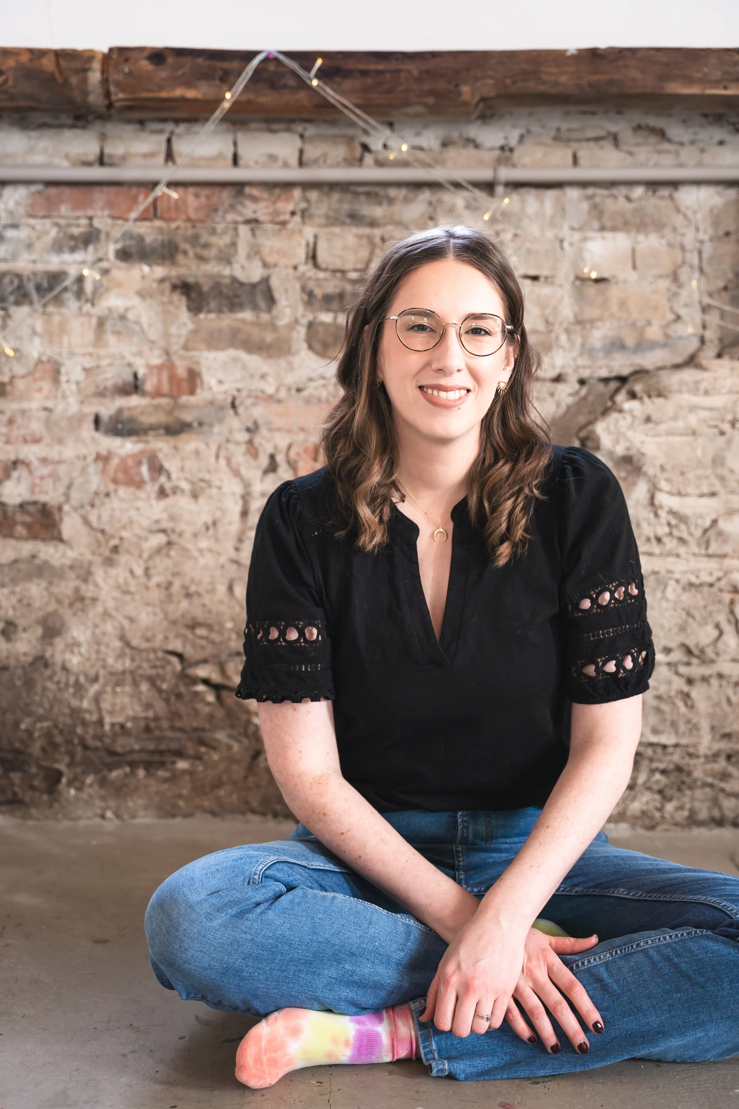 A female Toronto therapist for chronic GI conditions and disordered eating sitting cross-legged on concrete.