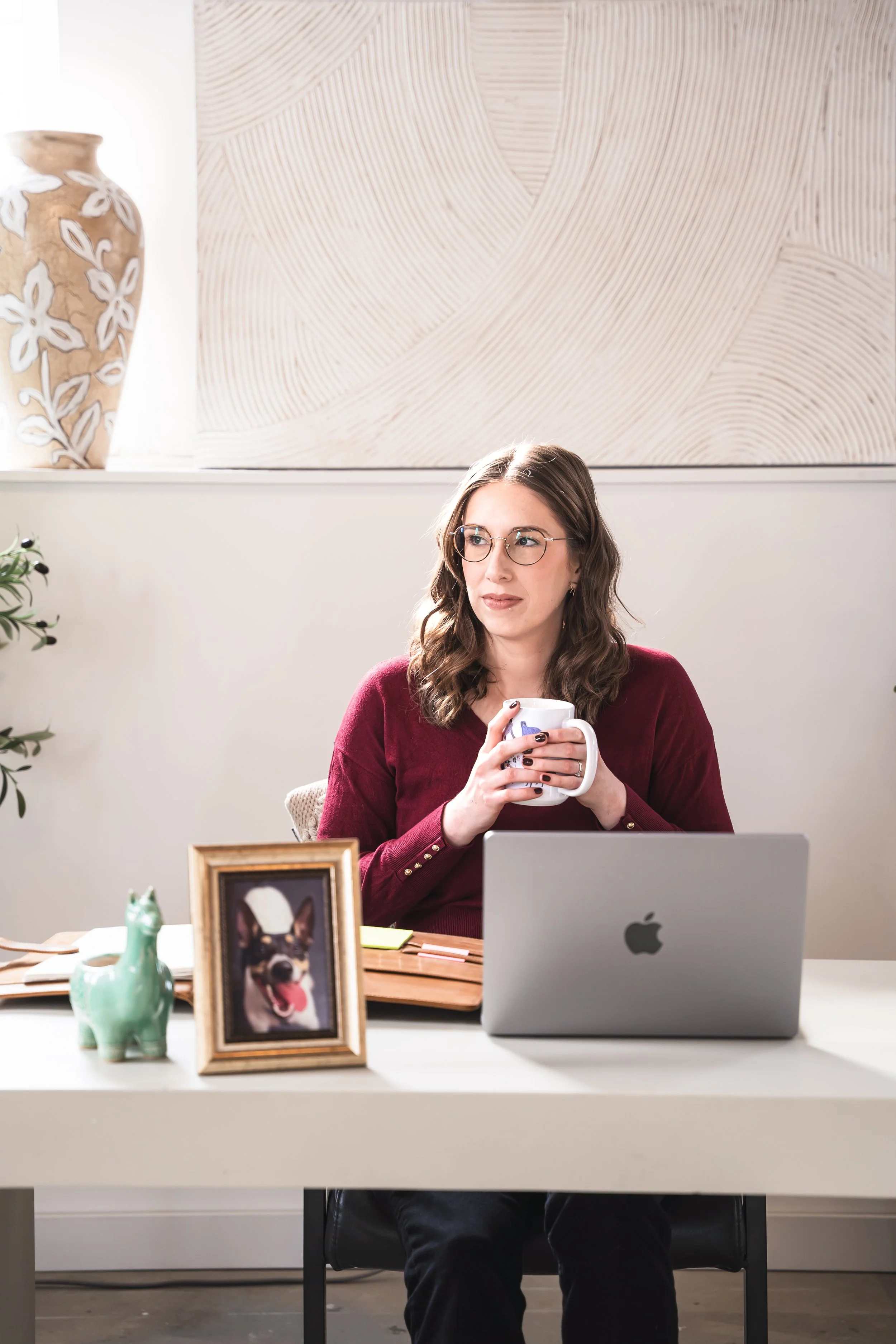 A therapist for disordered eating in Ontario holding a mug sitting at her desk behind a photo of her dog.