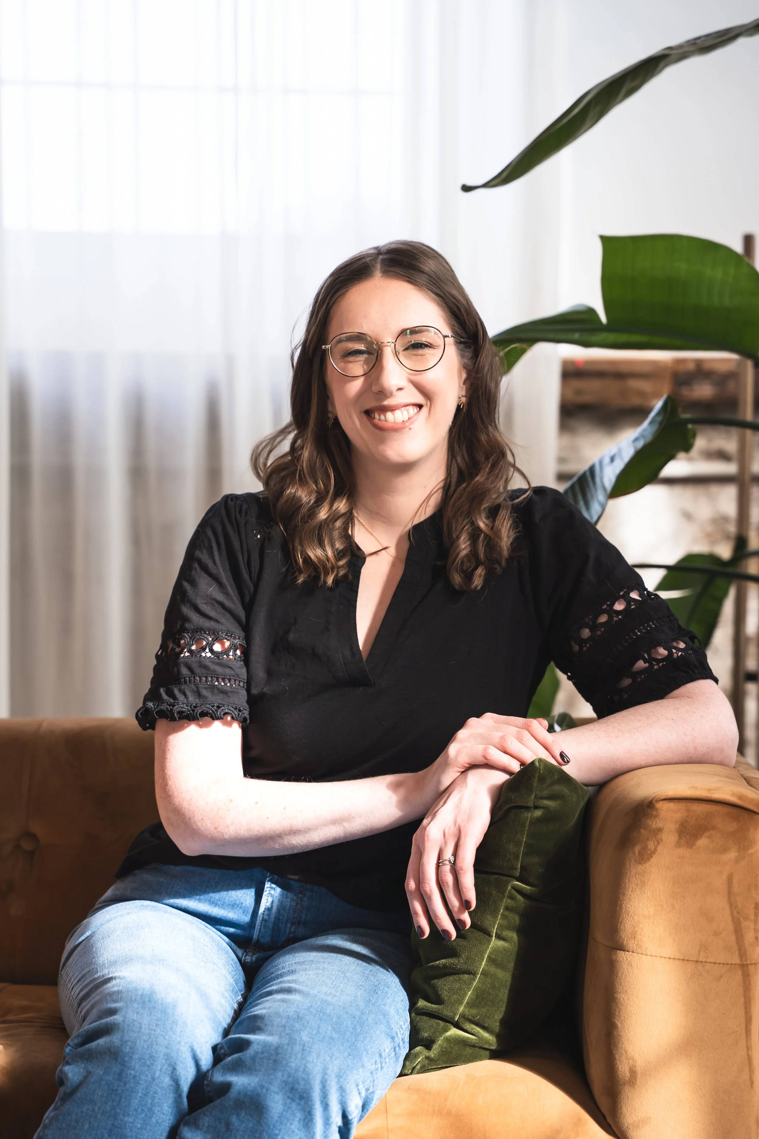A female Toronto therapist for IBS anxiety and disordered eating sitting on a brown suede couch smiling.