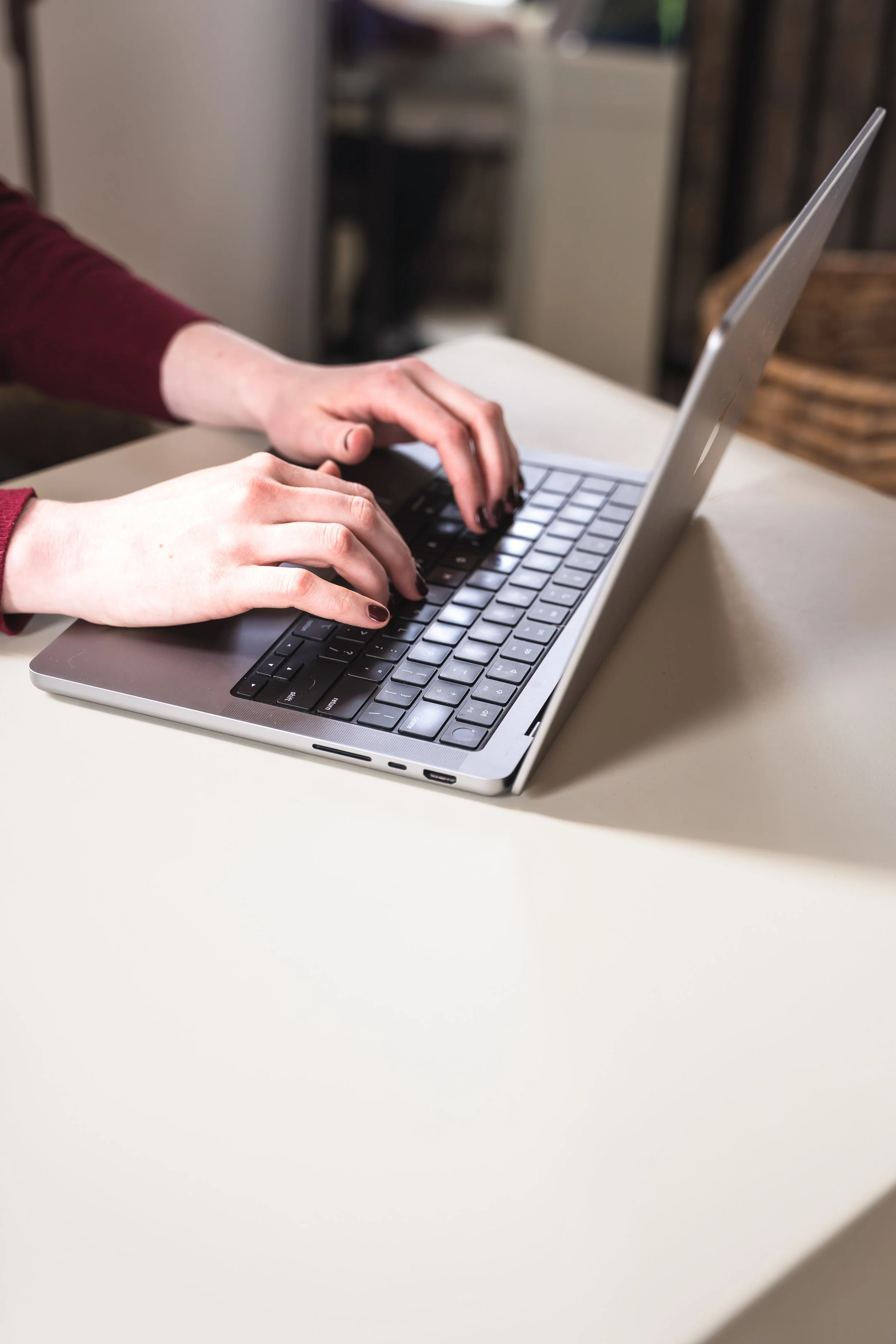 A therapist for chronic GI conditions in Toronto Ontario typing on her macbook with red nails.