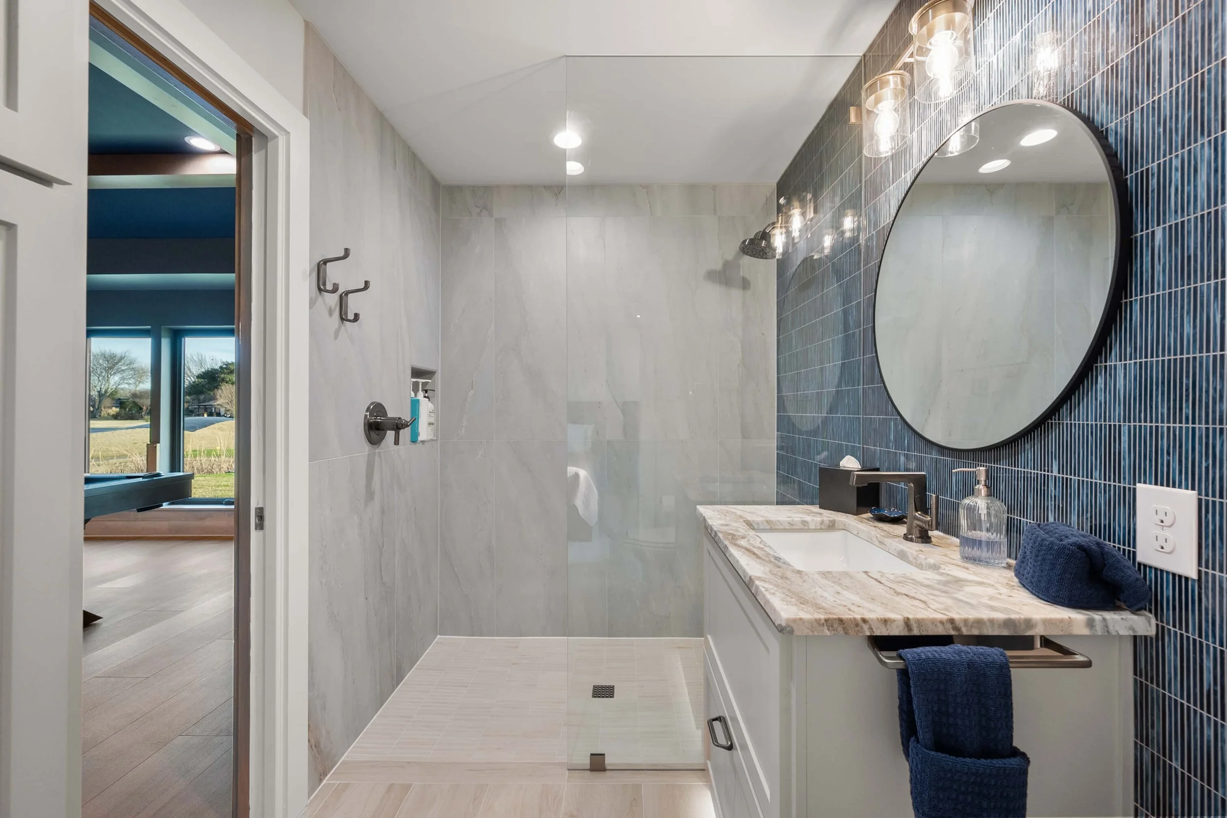 Modern bathroom with blue tile accent wall, large mirror, marble vanity, and walk-in shower with glass doors.