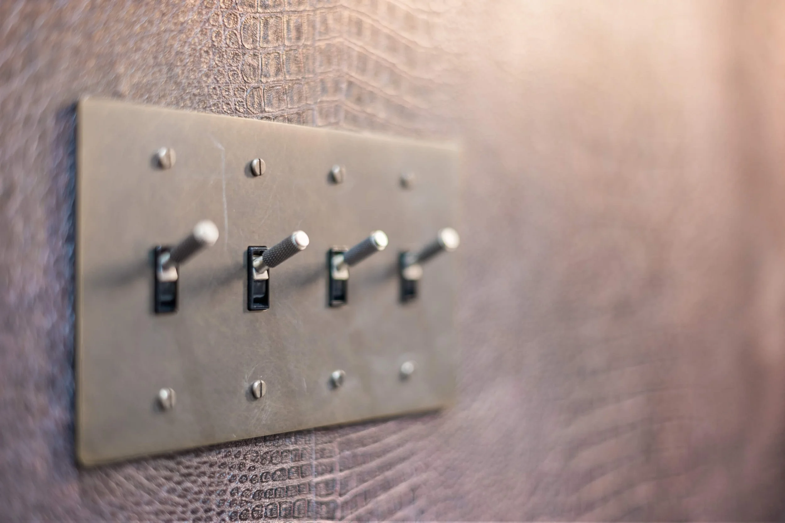 Close-up of a metallic panel with four switch toggles mounted on a textured wall.