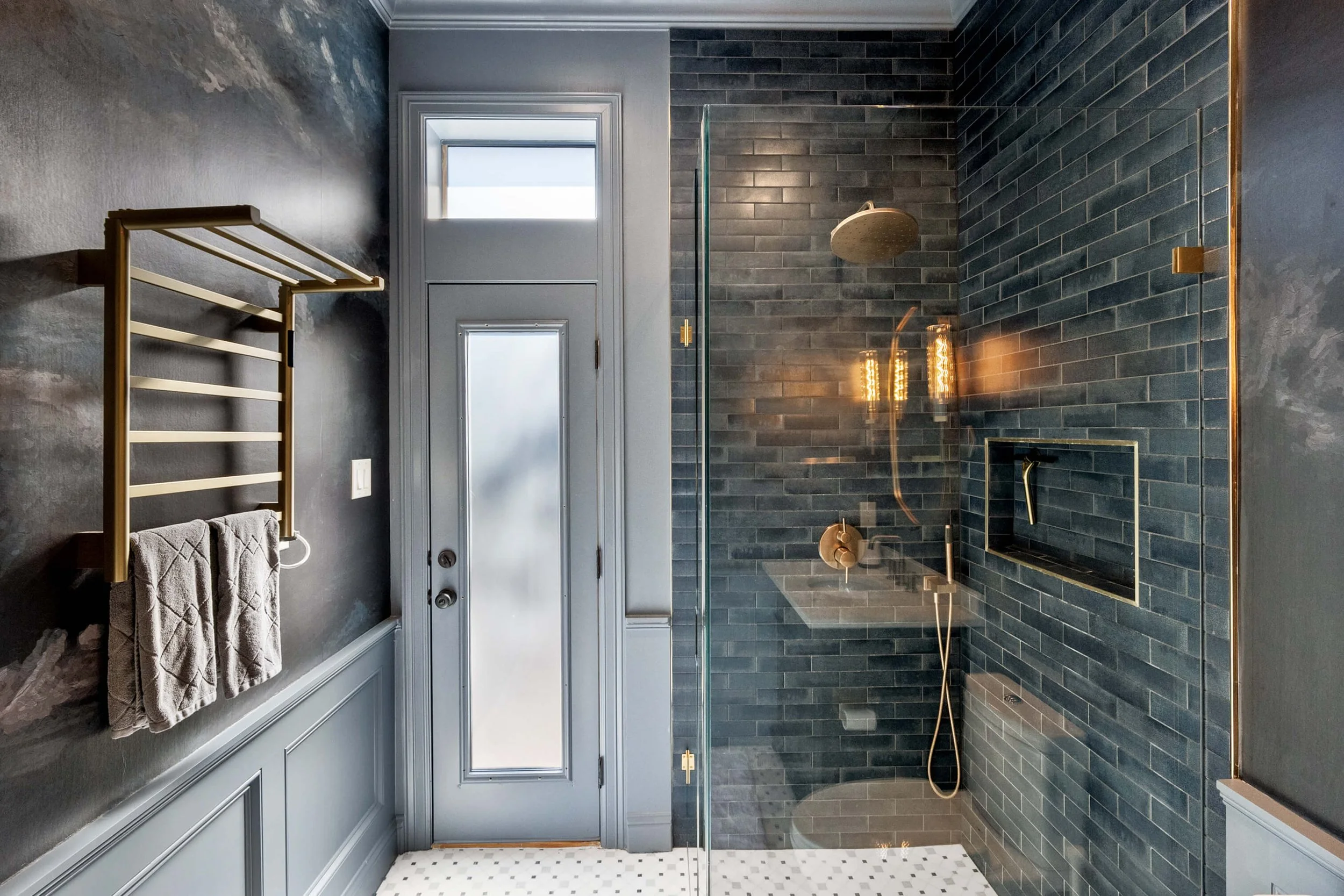 Modern bathroom with a glass-enclosed shower, dark gray tiled walls, a frosted glass door, and a towel rack with two beige towels.