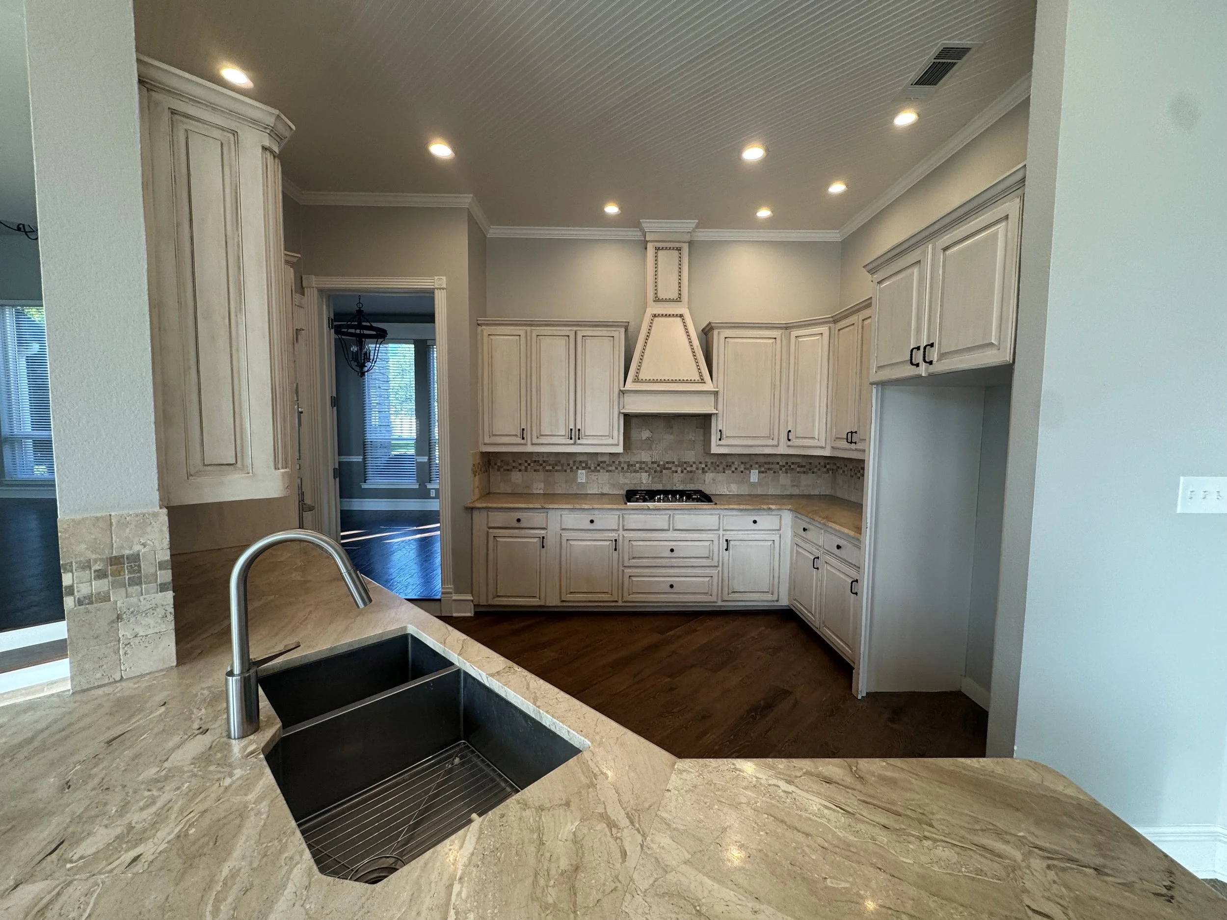 Kitchen with cream-colored cabinets, a beige marble countertop, a black sink, a stove, and a tiled backsplash, with hardwood flooring and recessed lighting.