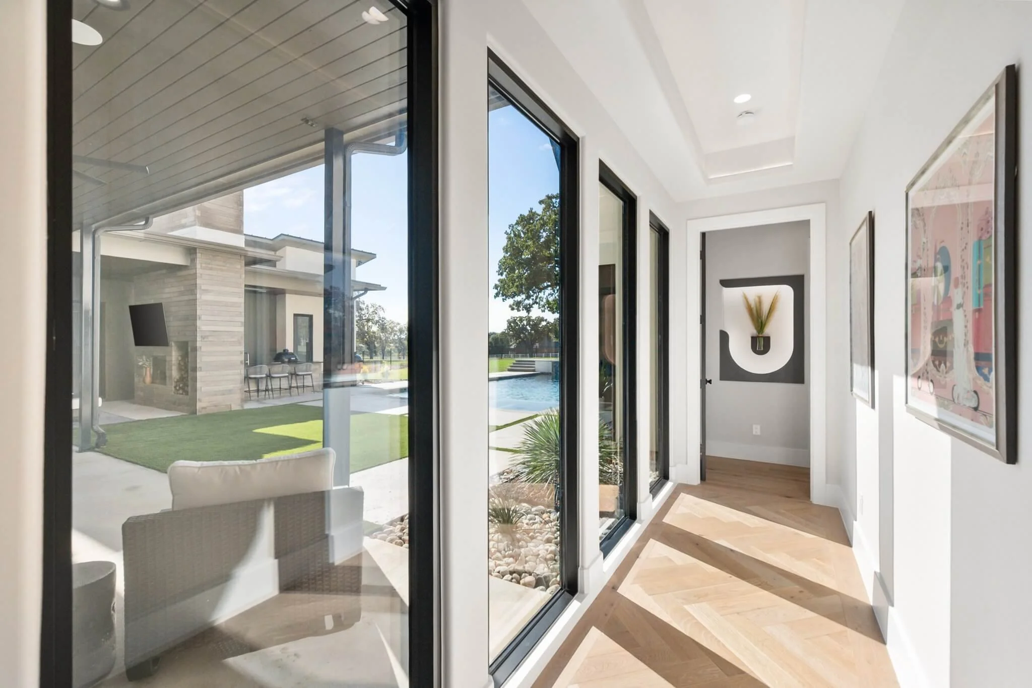 Bright interior hallway with large sliding glass doors and artwork on the wall, leading to an outdoor patio with a pool and landscaped yard.
