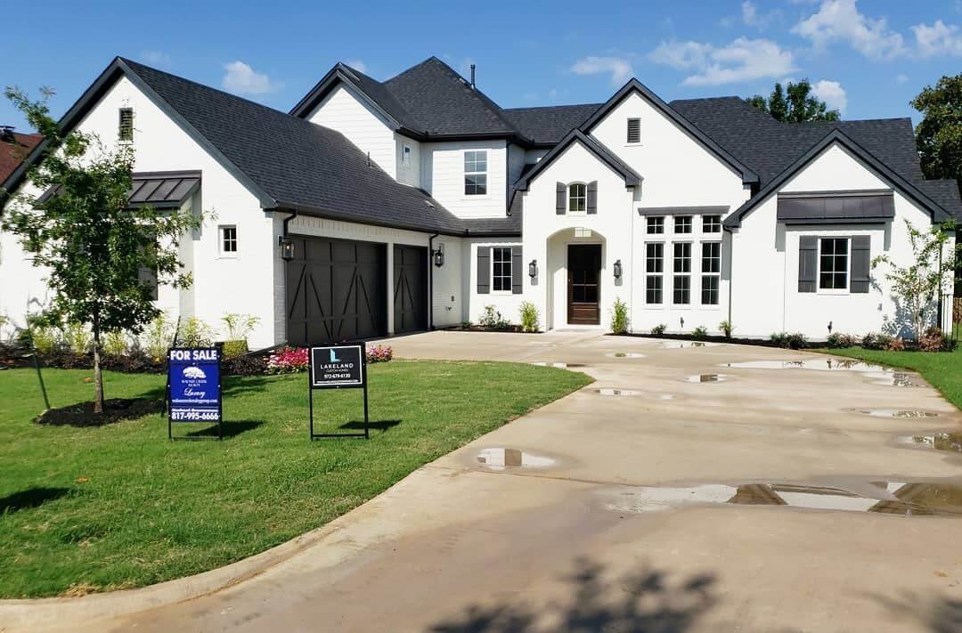 Modern two-story house with white exterior and black roof, front yard with green grass, small trees,  in Mansfield, TX.