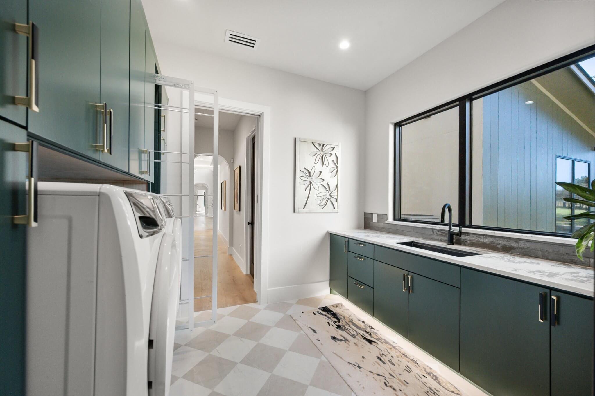 Modern laundry room with teal cabinets, a marble countertop, a large window, and white accents.