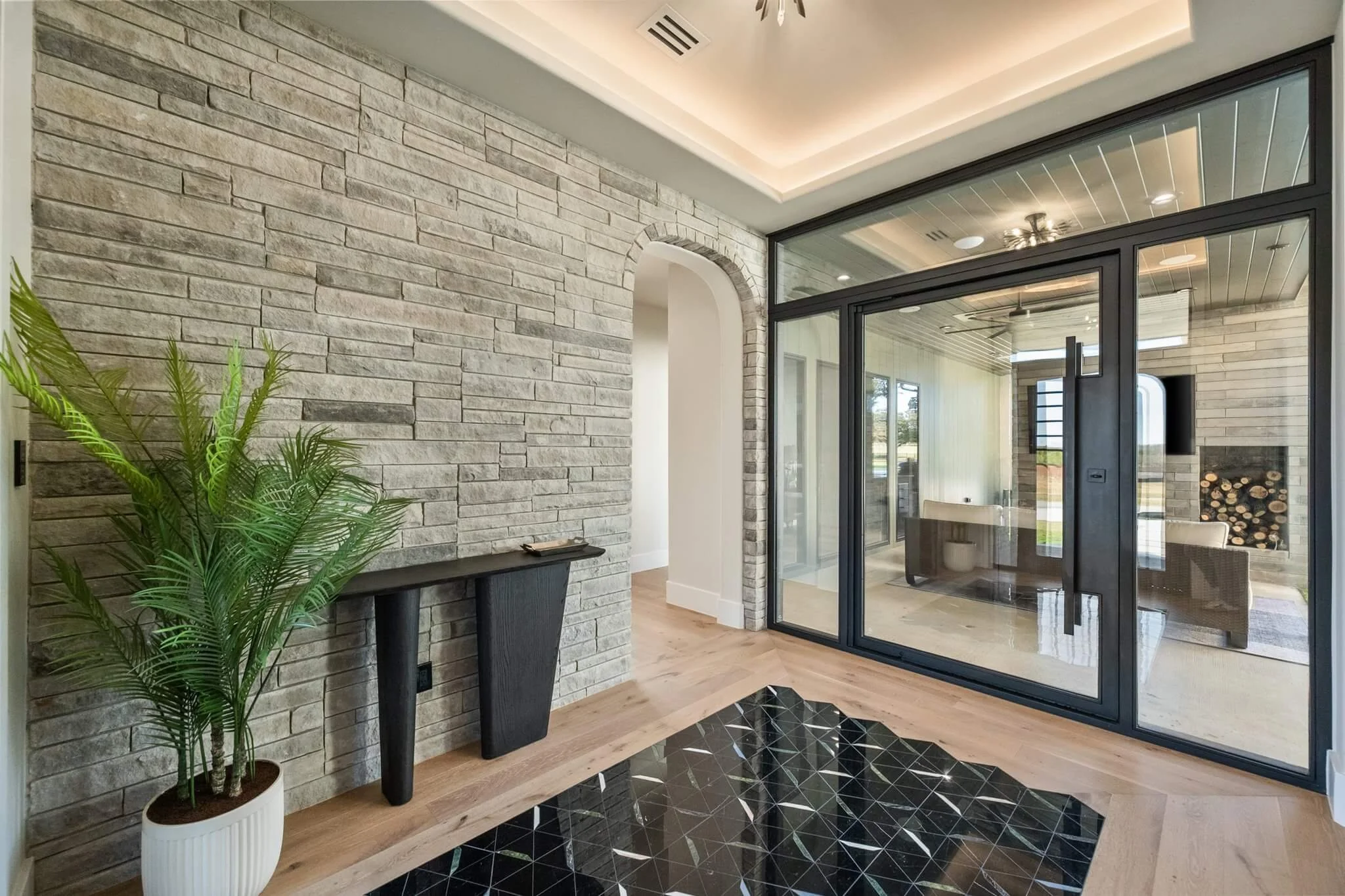 Interior living space with a stone accent wall, a large glass sliding door, a wooden floor, a black decorative rug, and a potted plant.
