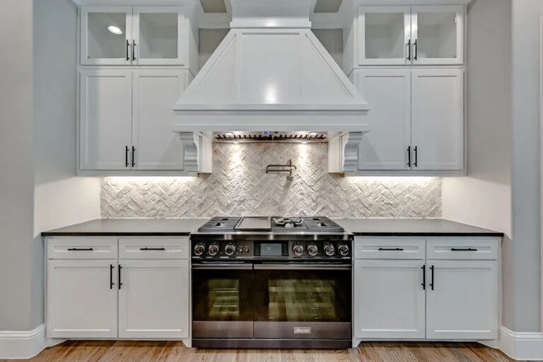 Modern kitchen with white cabinets, black handles, a black stove, and a textured backsplash under a white range hood in Mansfield, TX.