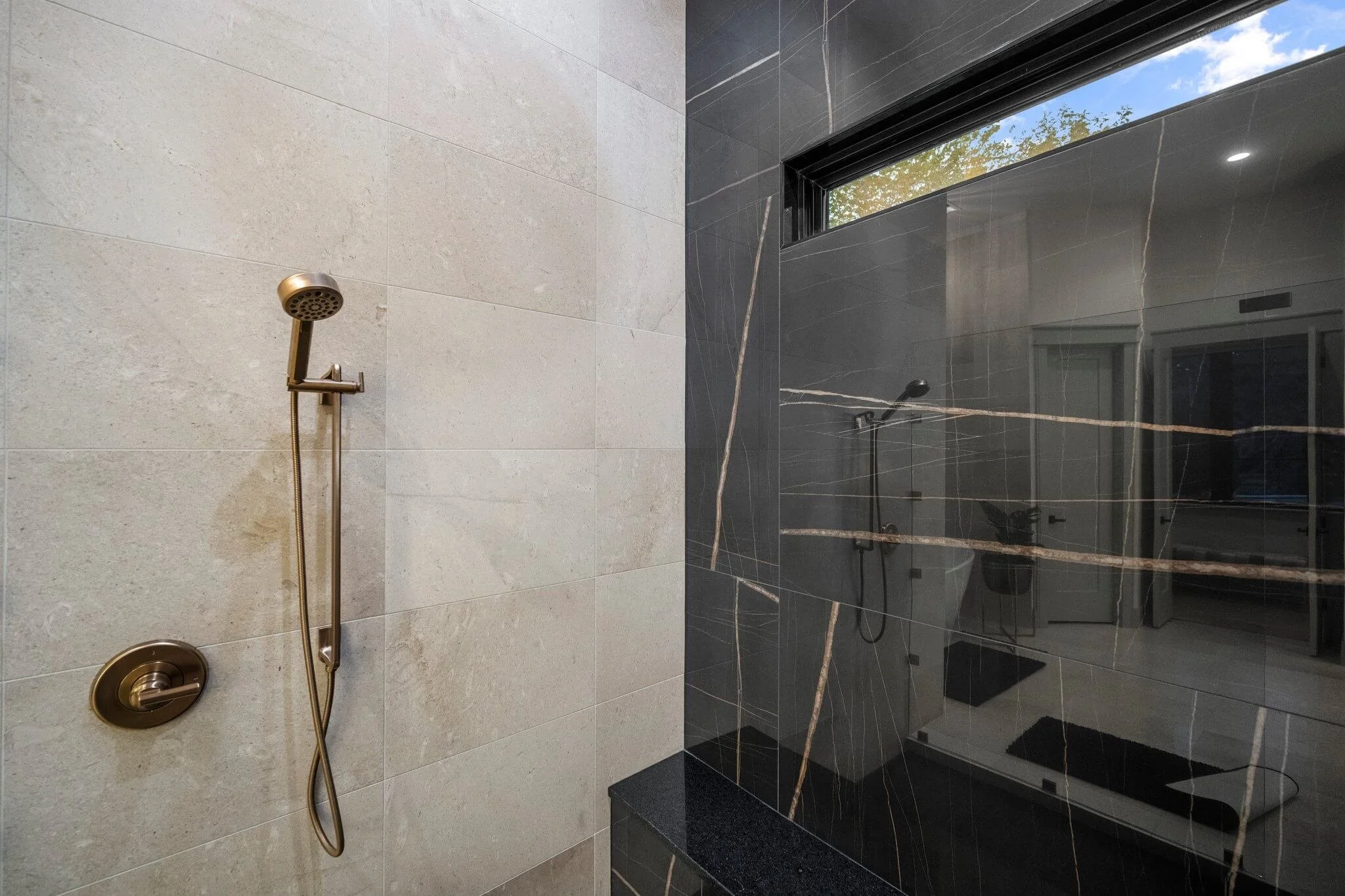 Modern bathroom with beige tile wall, black marble accent wall with gold veining, and a built-in shower with a handheld showerhead built by Lakeland Custom Homes.