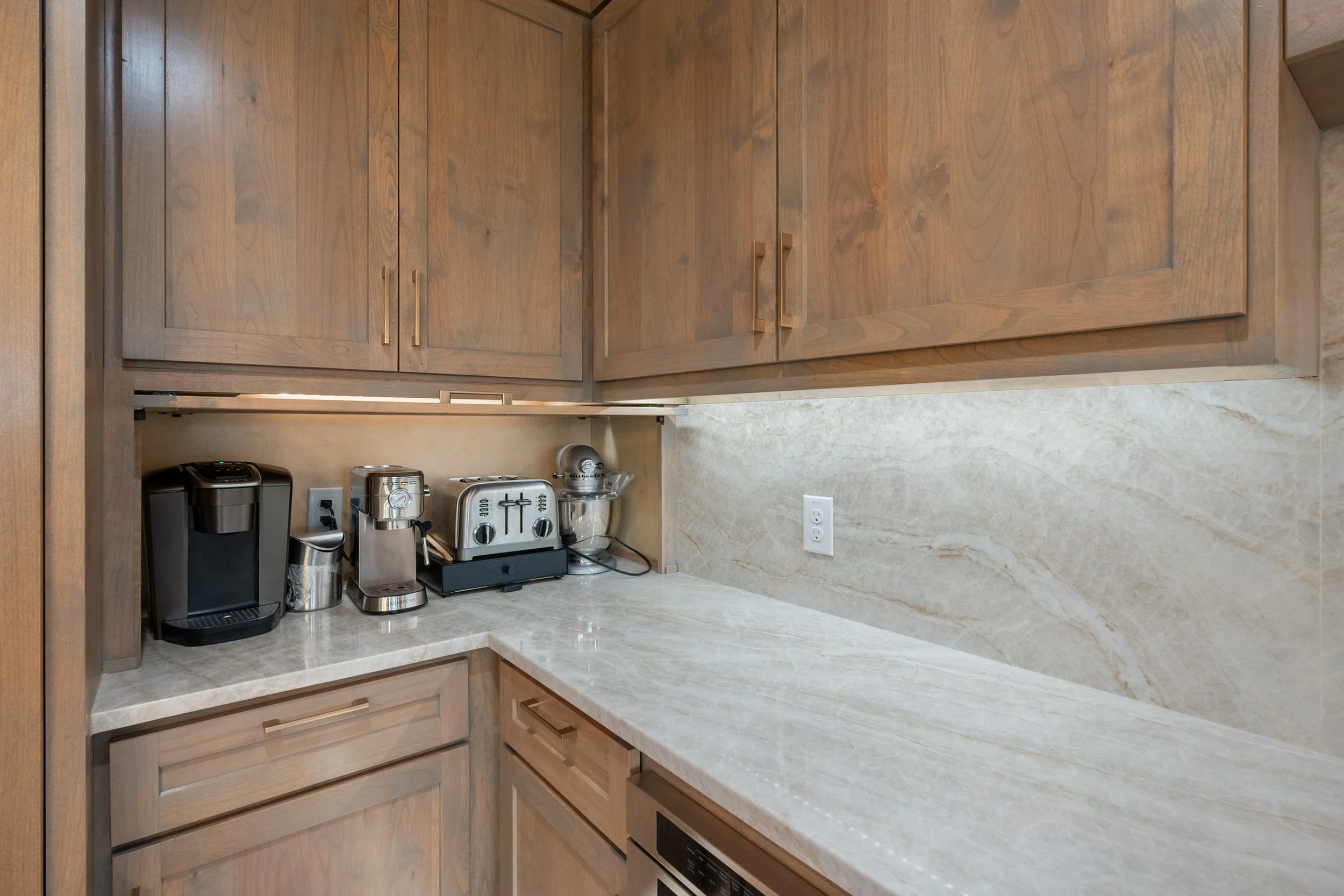 Kitchen counter with coffee maker, espresso machine, toaster, and stand mixer against wooden cabinets and marble backsplash built by Lakeland Custom Homes.