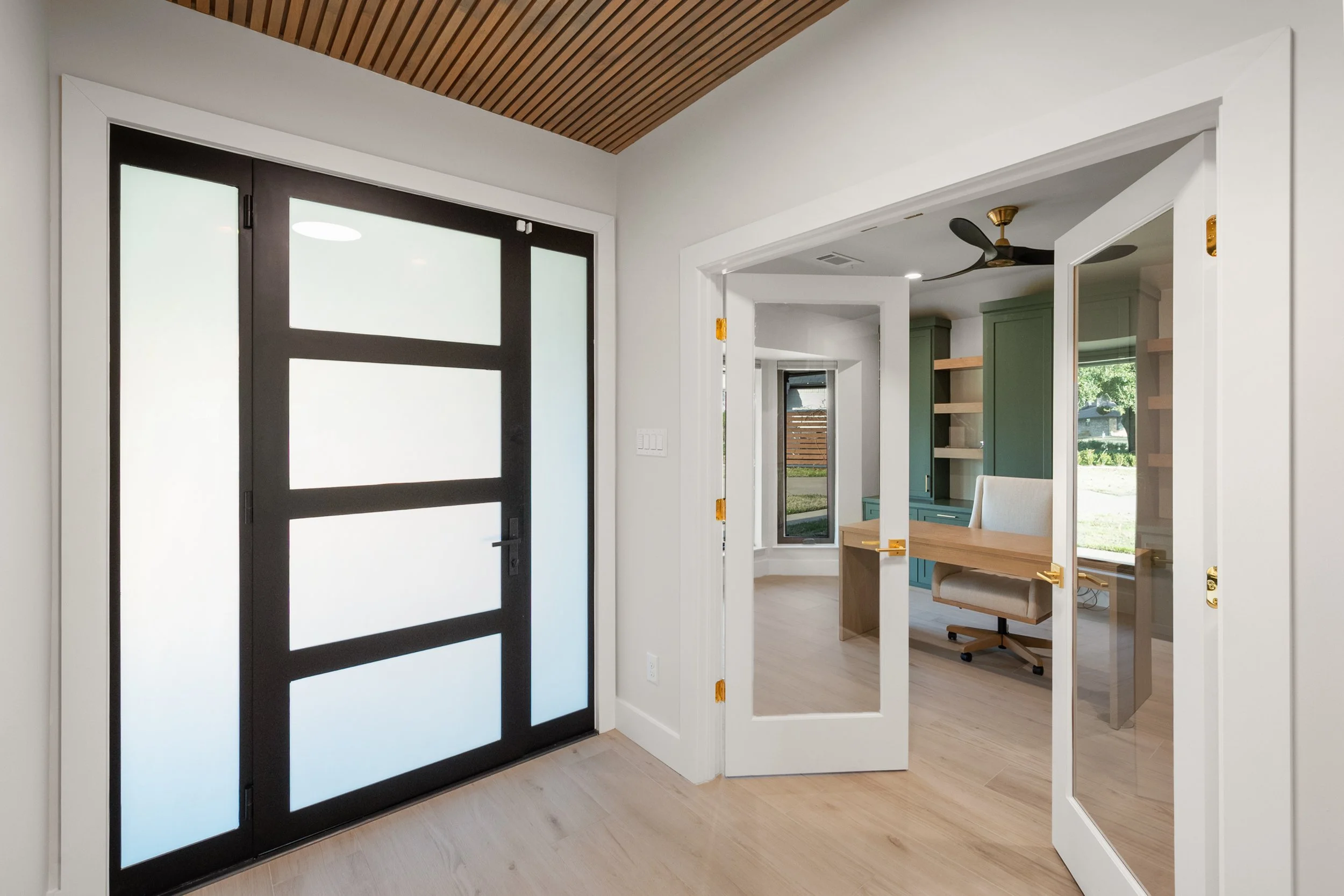 Modern home interior with black sliding door, white interior walls, and a view into a room with green cabinets, wooden shelves, and a desk.