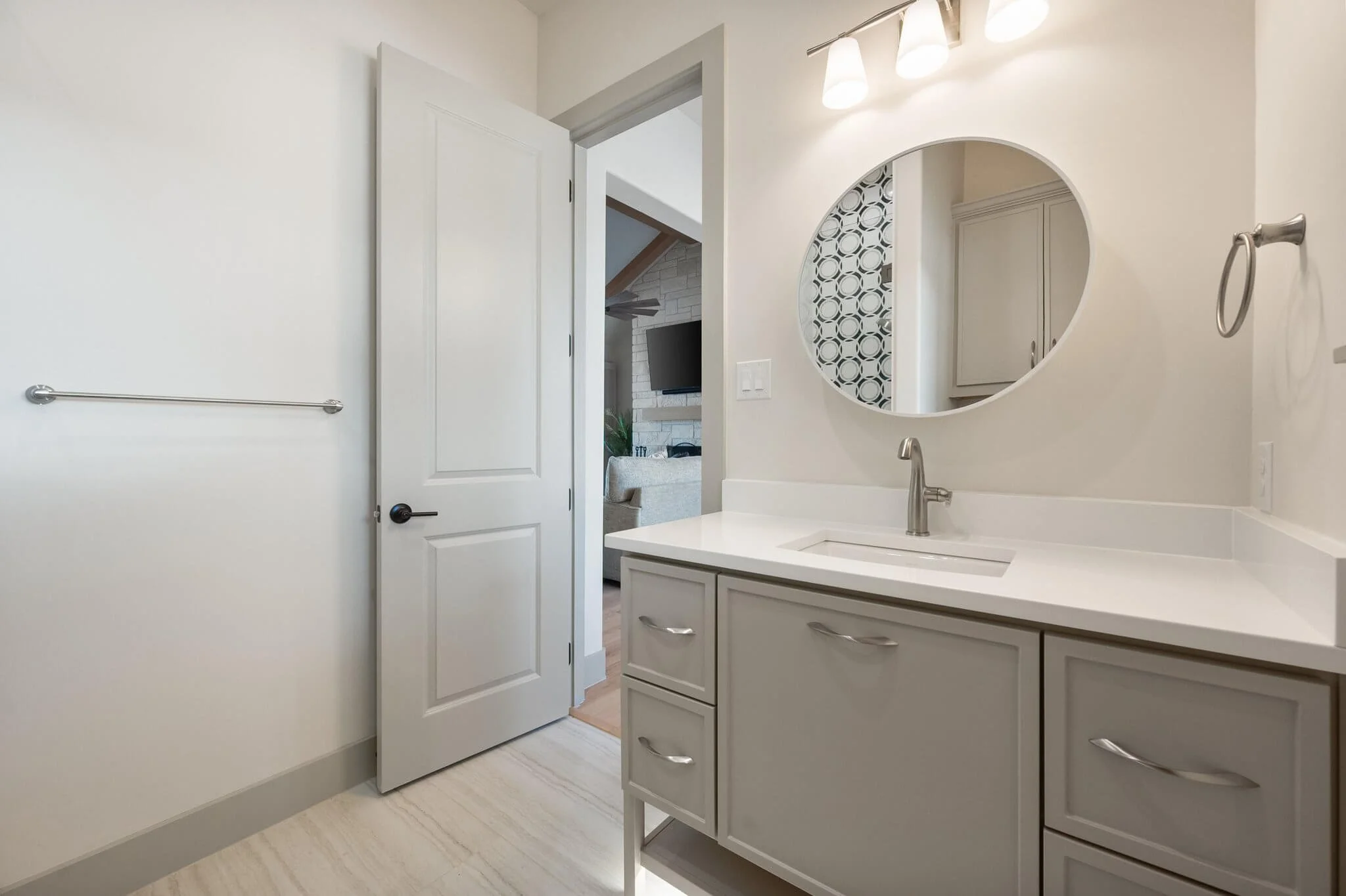 Bathroom vanity with a white countertop, a mirror, and a faucet, with a view into a living room through an open door built by Lakeland Custom Homes.