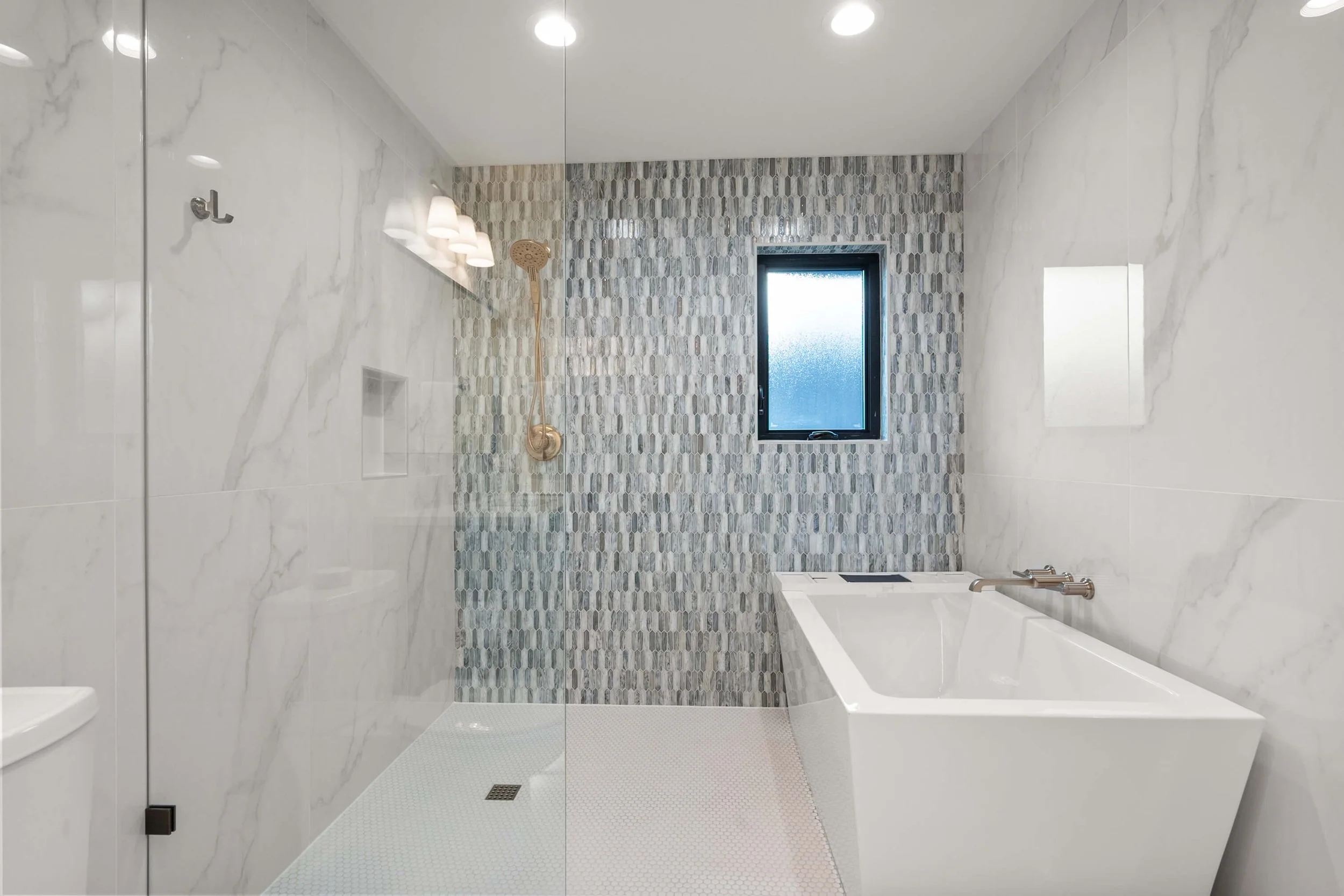 Modern bathroom with a walk-in shower featuring a yellow showerhead and mosaic tiled wall, a white bathtub, white marble wall tiles, a frosted window, and ceiling lights.