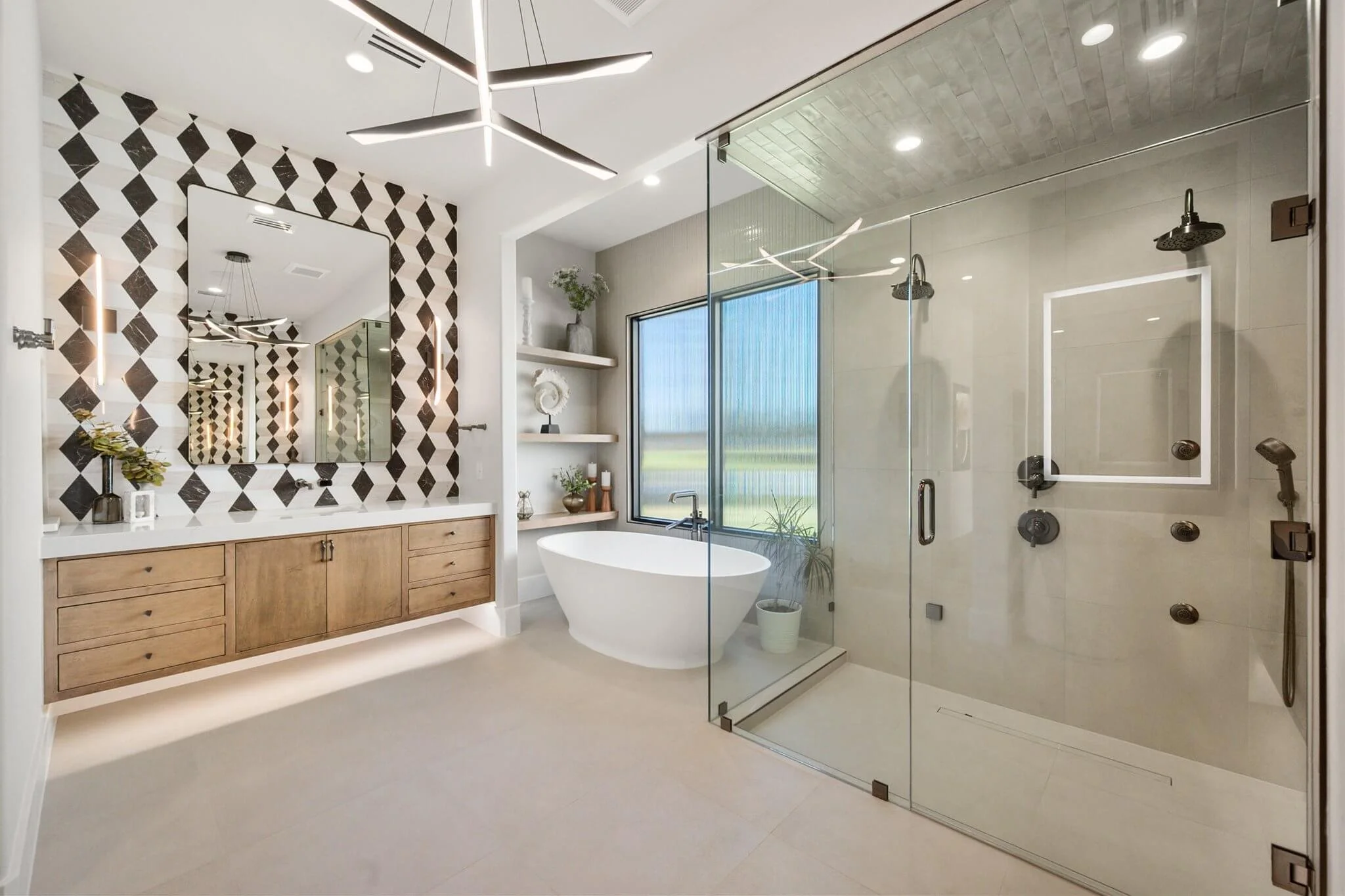 Modern bathroom with a walk-in glass shower, freestanding bathtub, wooden vanity with a geometric black-and-white tiled wall, and decorative shelving with plants and accessories.