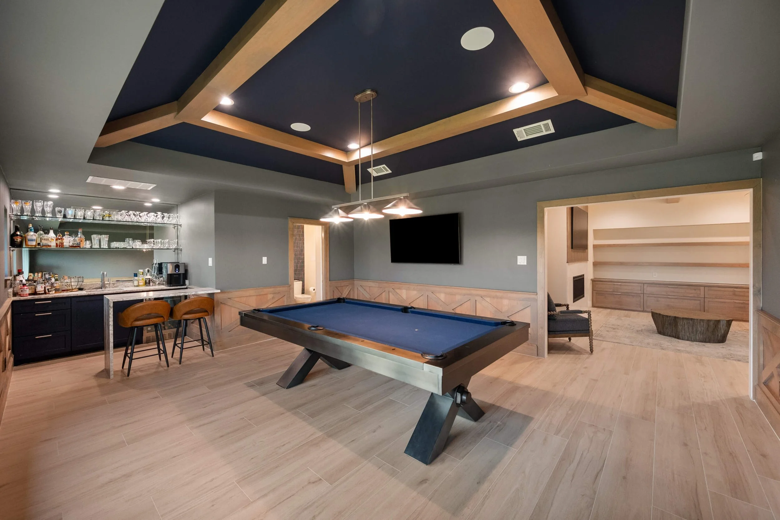 A modern recreational room with a pool table, a bar area, a TV mounted on the wall, and a cozy seating nook built by Lakeland Custom Homes.