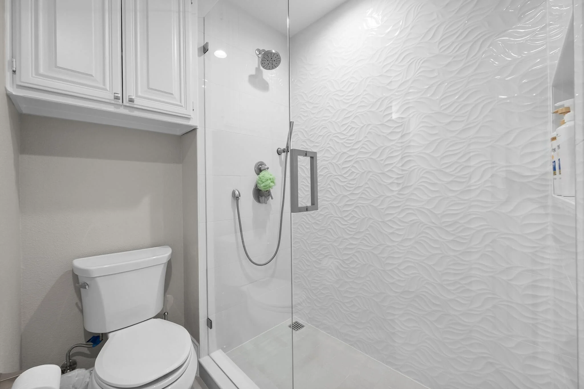 A modern bathroom with a white toilet and a walk-in shower with textured white wall tiles and a glass door.