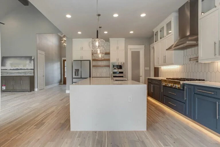 Modern kitchen with white cabinetry, a large white island, blue lower cabinets, stainless steel appliances, and pendant lighting.