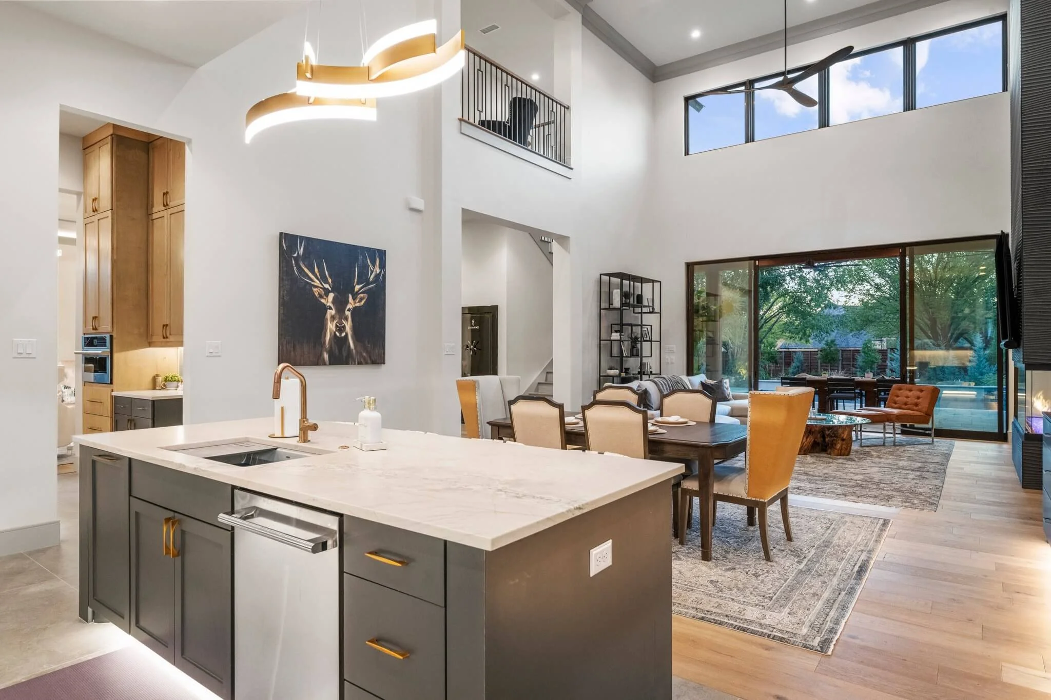  Modern kitchen design featuring marble countertops in a luxury home in Colleyville, TX. Open-concept living and dining area with large windows, high ceiling, modern furniture, and a kitchen island with a sink.