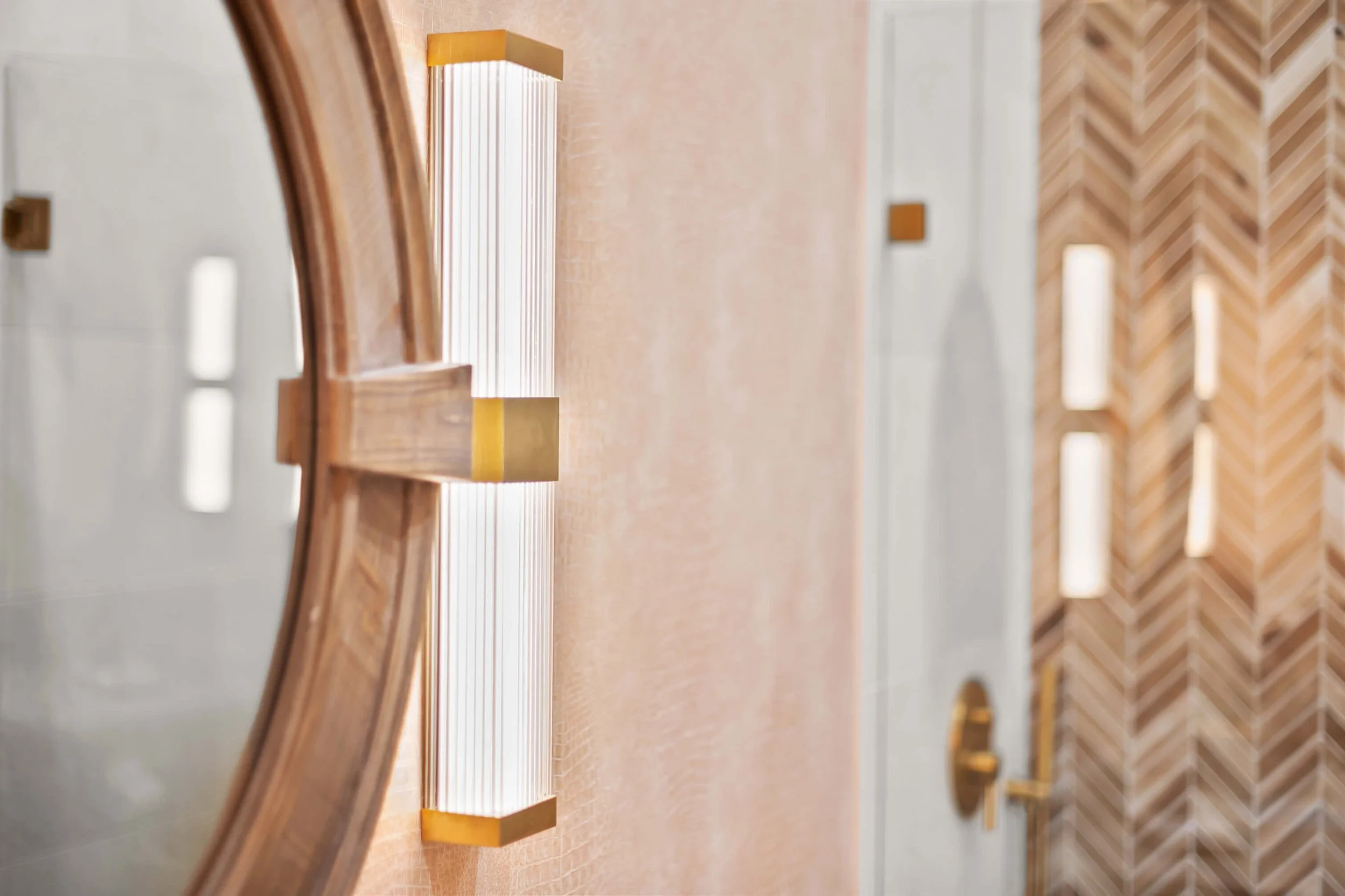 Close-up of a modern wall-mounted light fixture with a wood frame and frosted glass in a contemporary interior hallway, wall with textured design and a door with gold hardware in background.