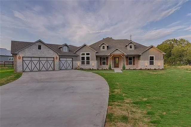Large modern house with a curved driveway, a two-car garage, and a front yard with grass under a partly cloudy sky.