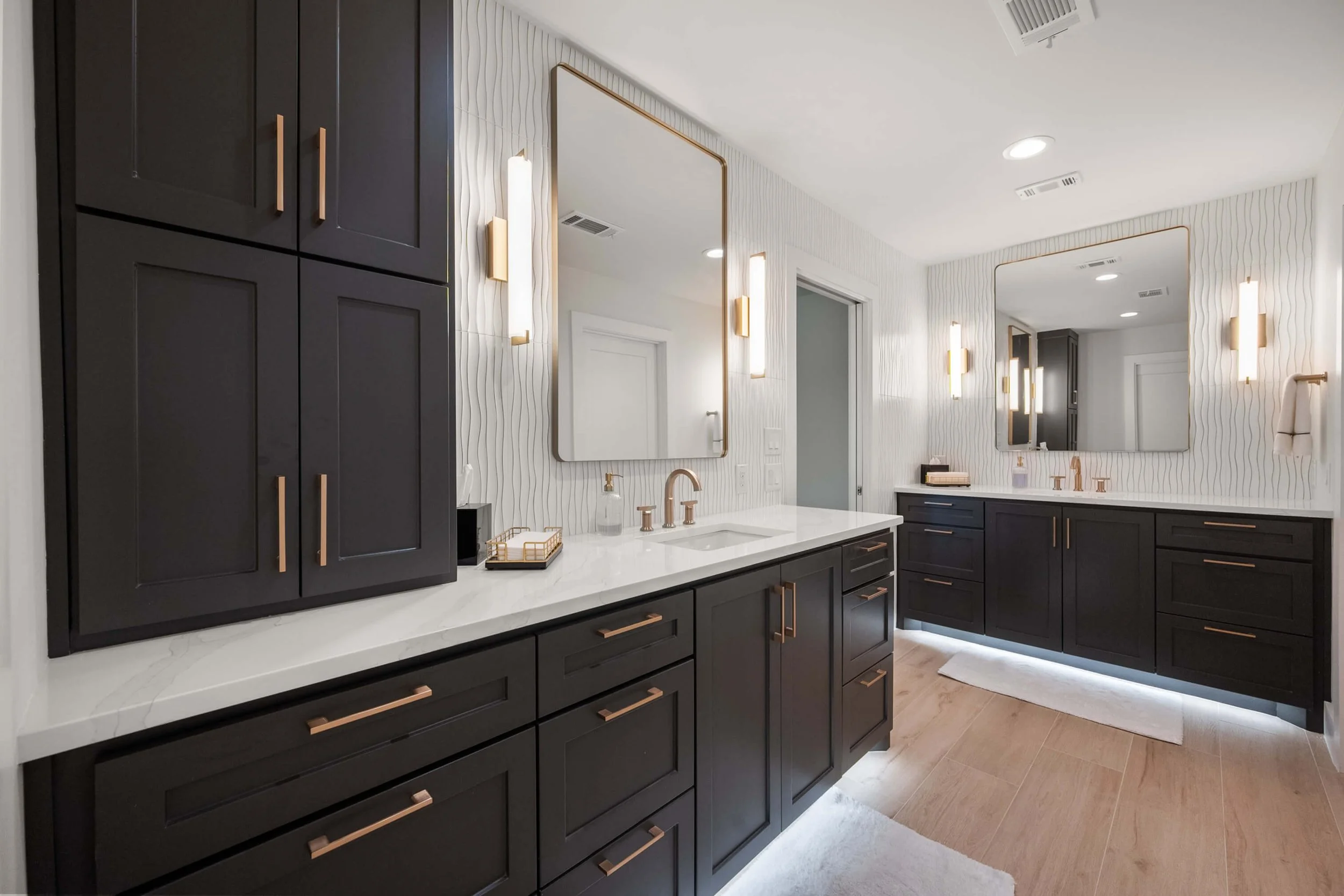 A modern bathroom with dark cabinetry, white countertops, large mirrors, and gold fixtures built by Lakeland Custom Homes.