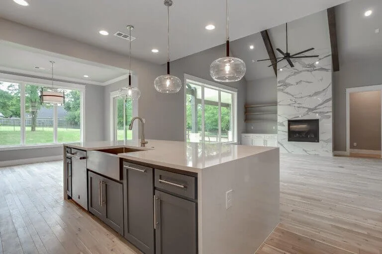 Modern open-concept kitchen and living room with large windows, pendant lights, front fireplace, and light-colored flooring in Mansfield, TX.