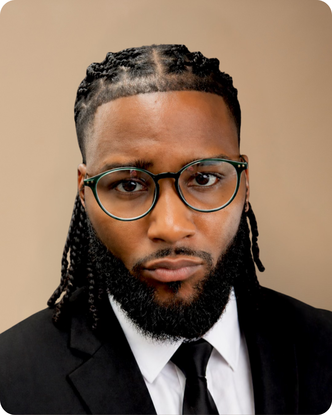 A man with braided hair, glasses, and a beard wearing a suit and tie.