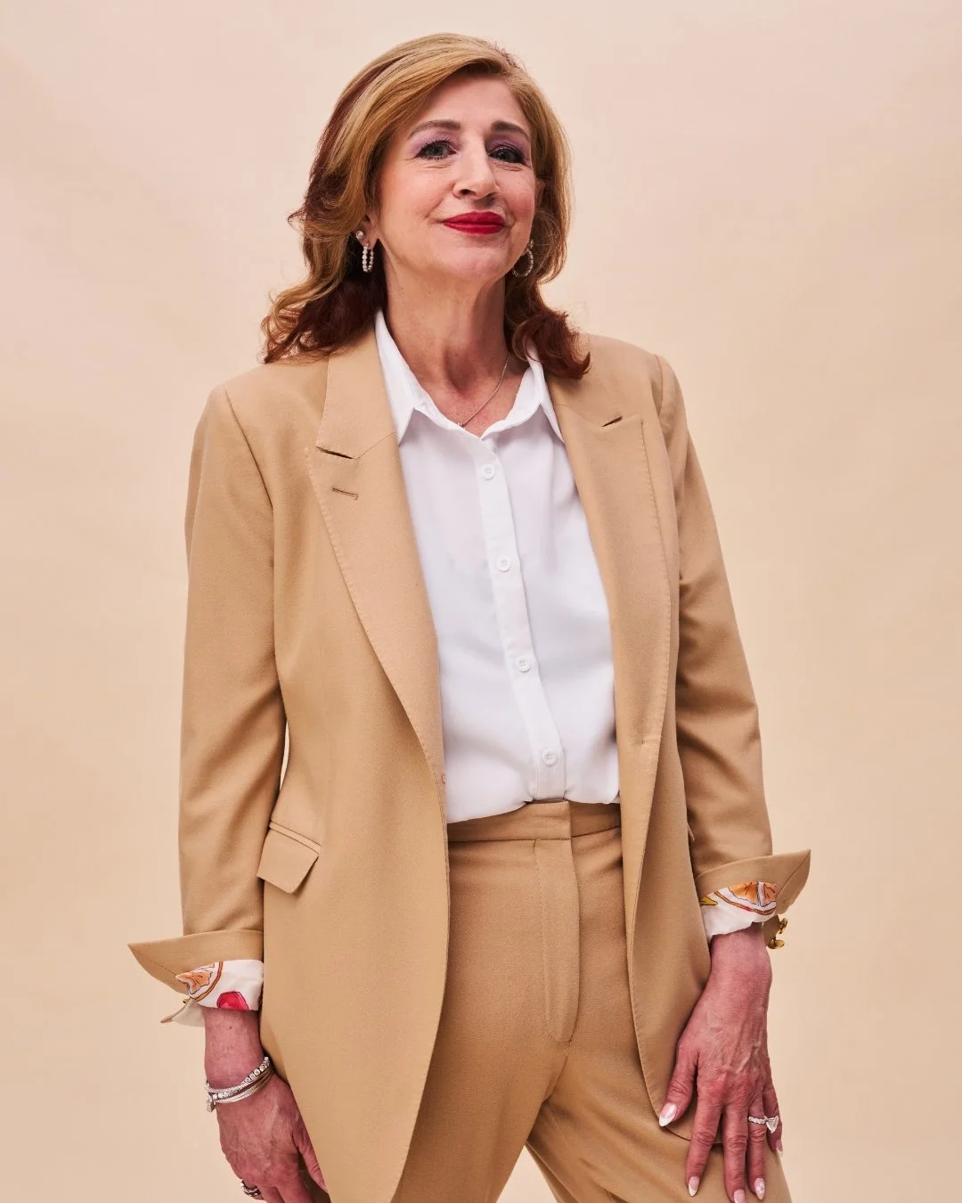 Melanie French, CEO of RR Living - A confident middle-aged woman with shoulder-length red hair, wearing a beige suit and white shirt, standing against a plain beige background.