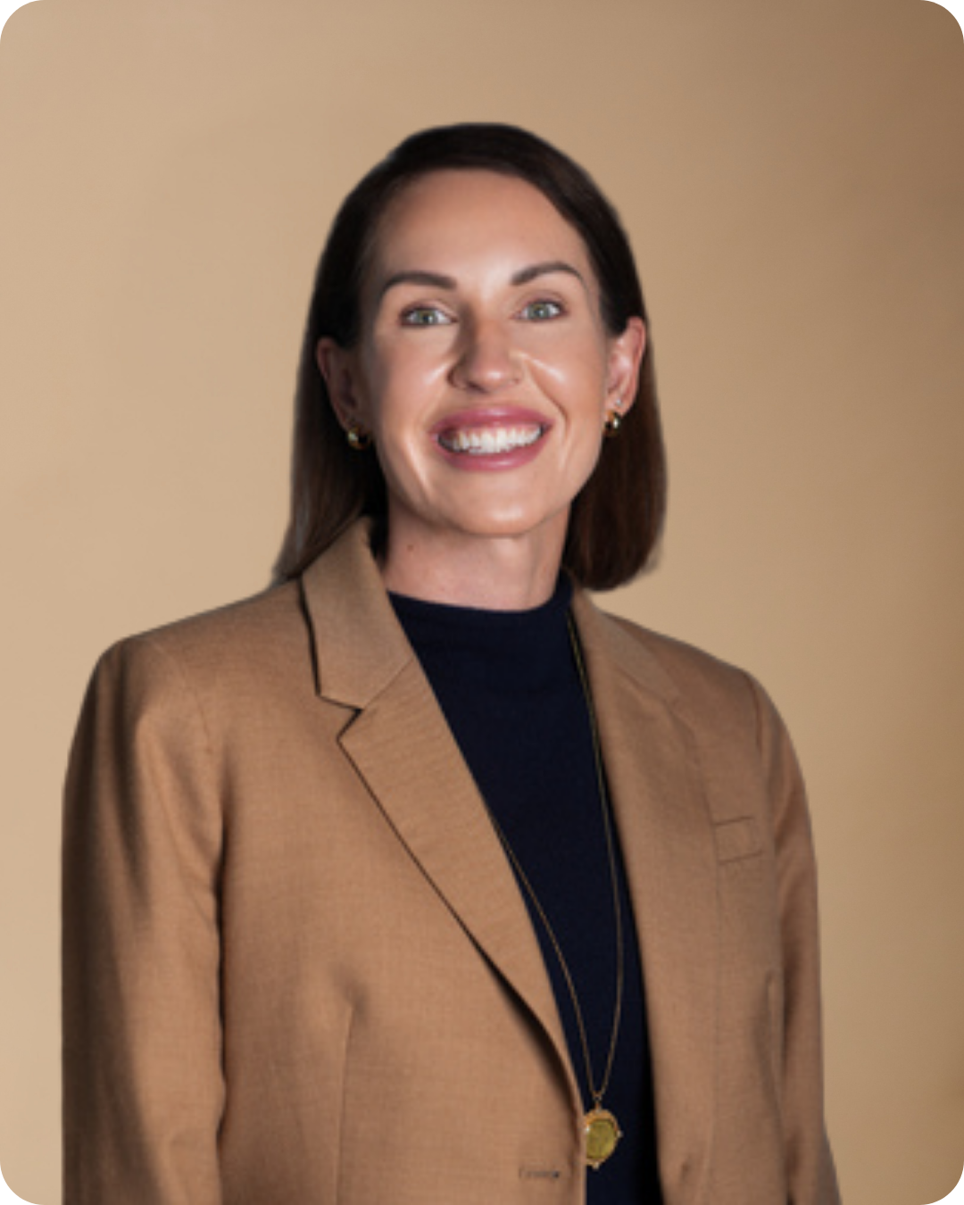 A professional woman with shoulder-length brown hair, wearing a beige blazer over a black top, smiling against a plain beige background.