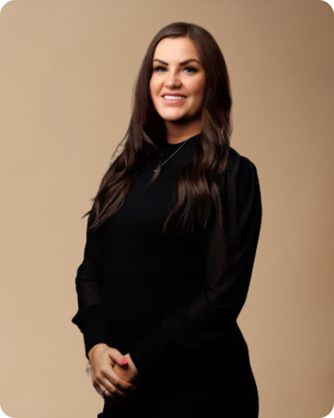 A woman with long brown hair wearing a black top, posing against a beige background.