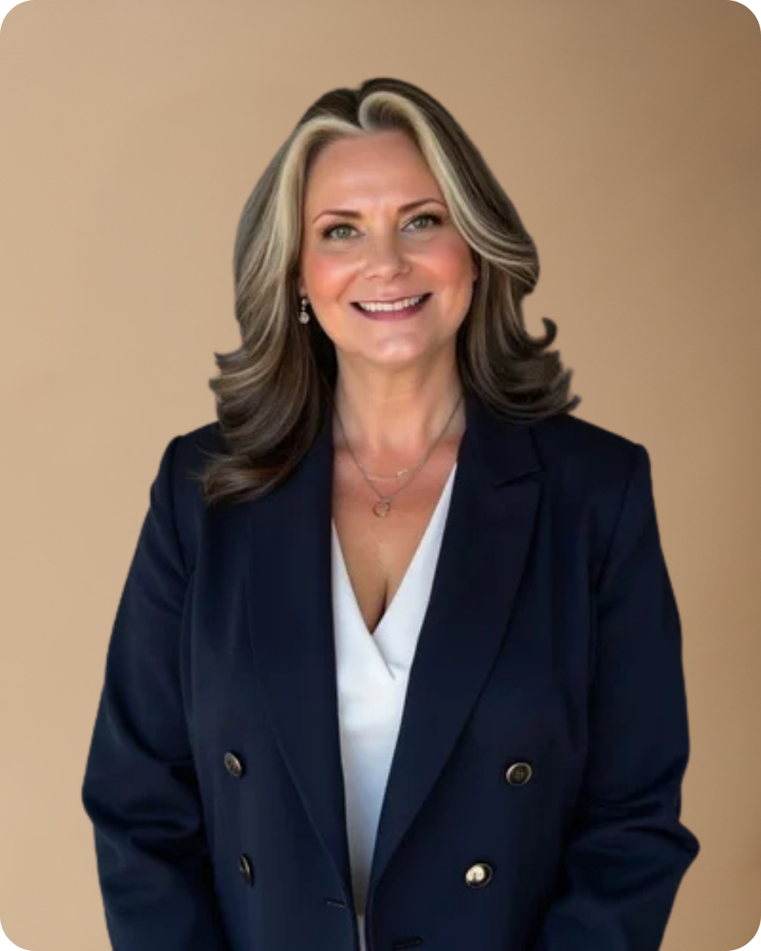 A woman with shoulder-length, wavy, gray and blonde hair, smiling and wearing a navy blazer over a white top, with jewelry, against a beige background.