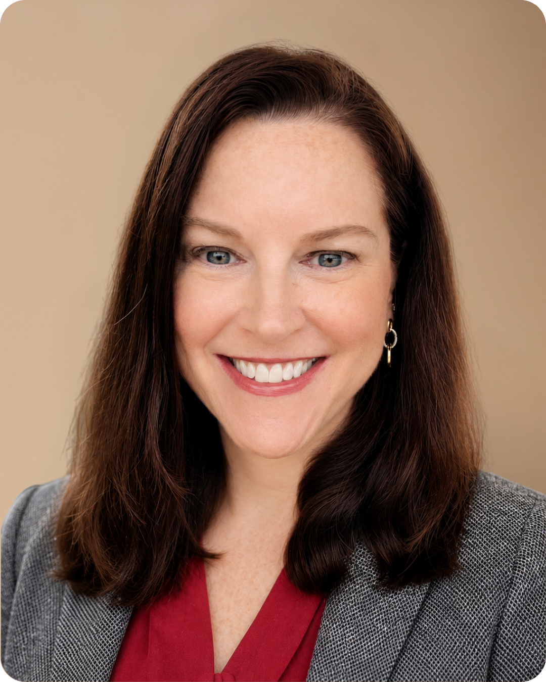 A professional woman with shoulder-length brown hair, wearing a light blue blazer and a floral blouse, smiling against a beige background.