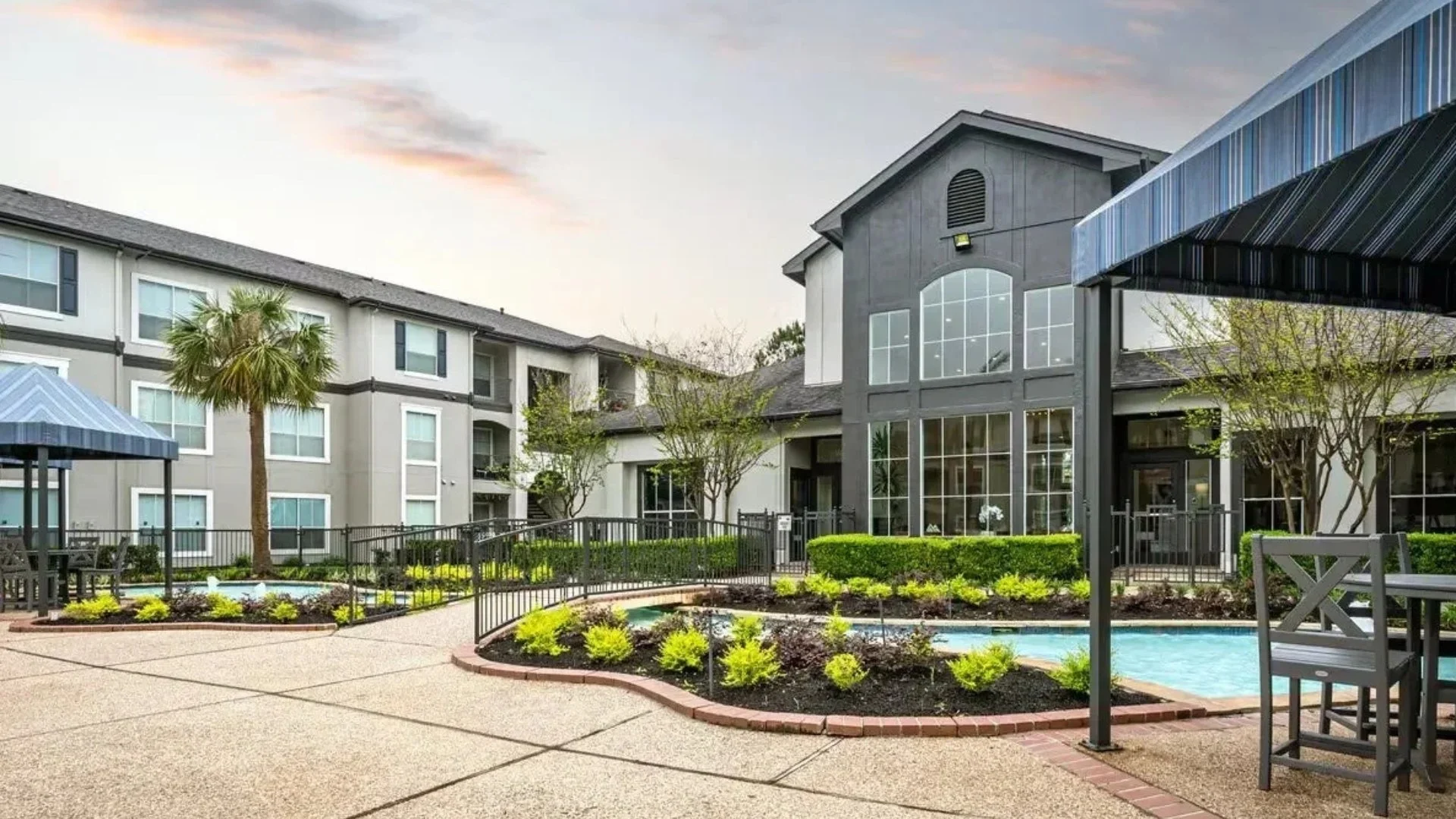 Exterior view of a modern apartment complex with landscaped yard, small pool, and walkways, during daytime.