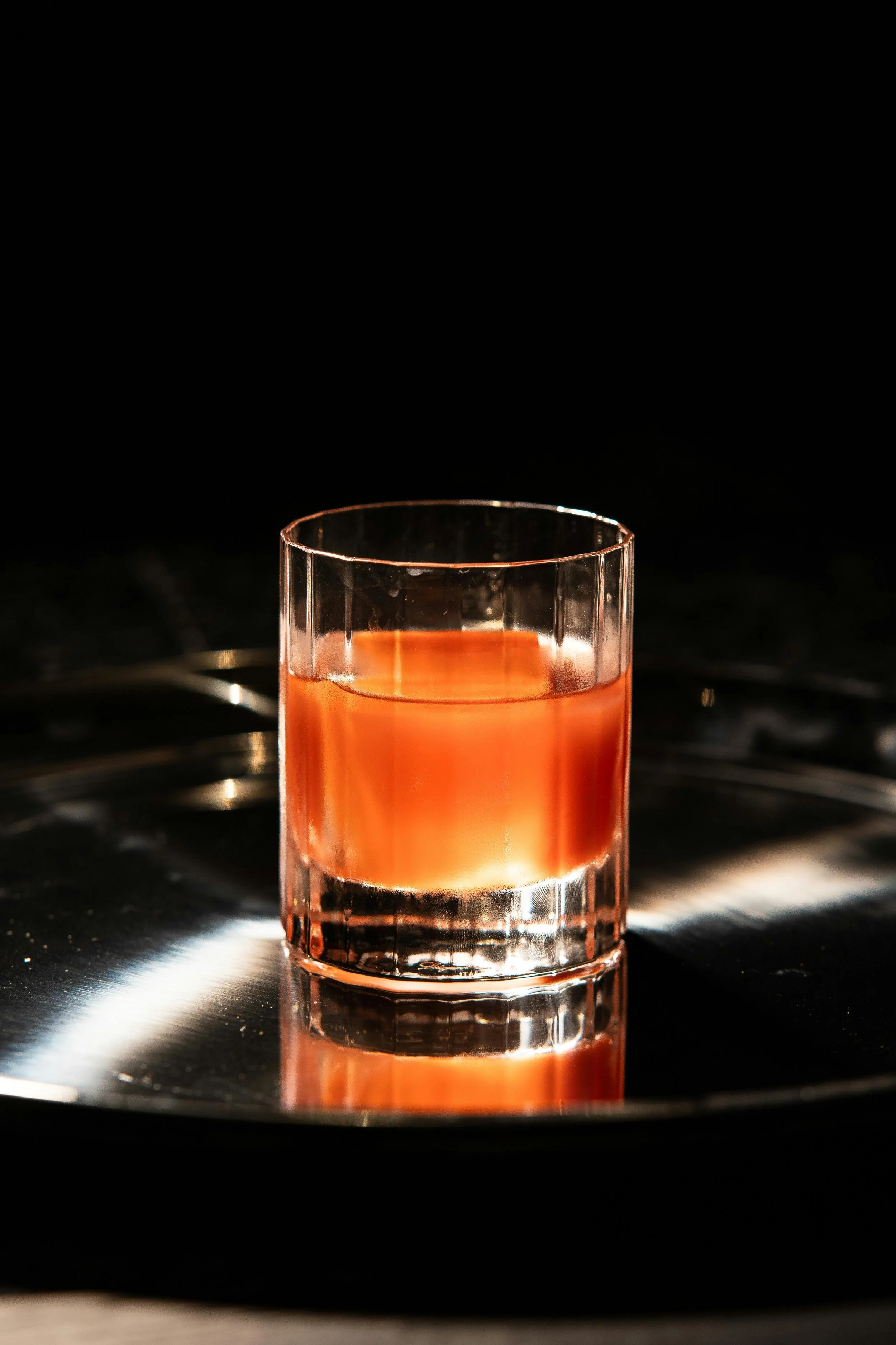 A glass of rosé wine on a reflective black surface with a dark background.