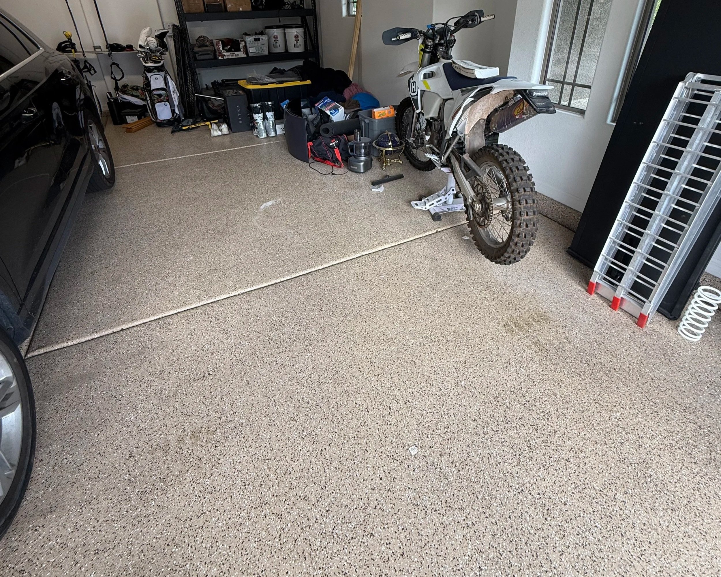 A garage interior with a dirt bike, tools, storage shelves, and a black car parked inside.