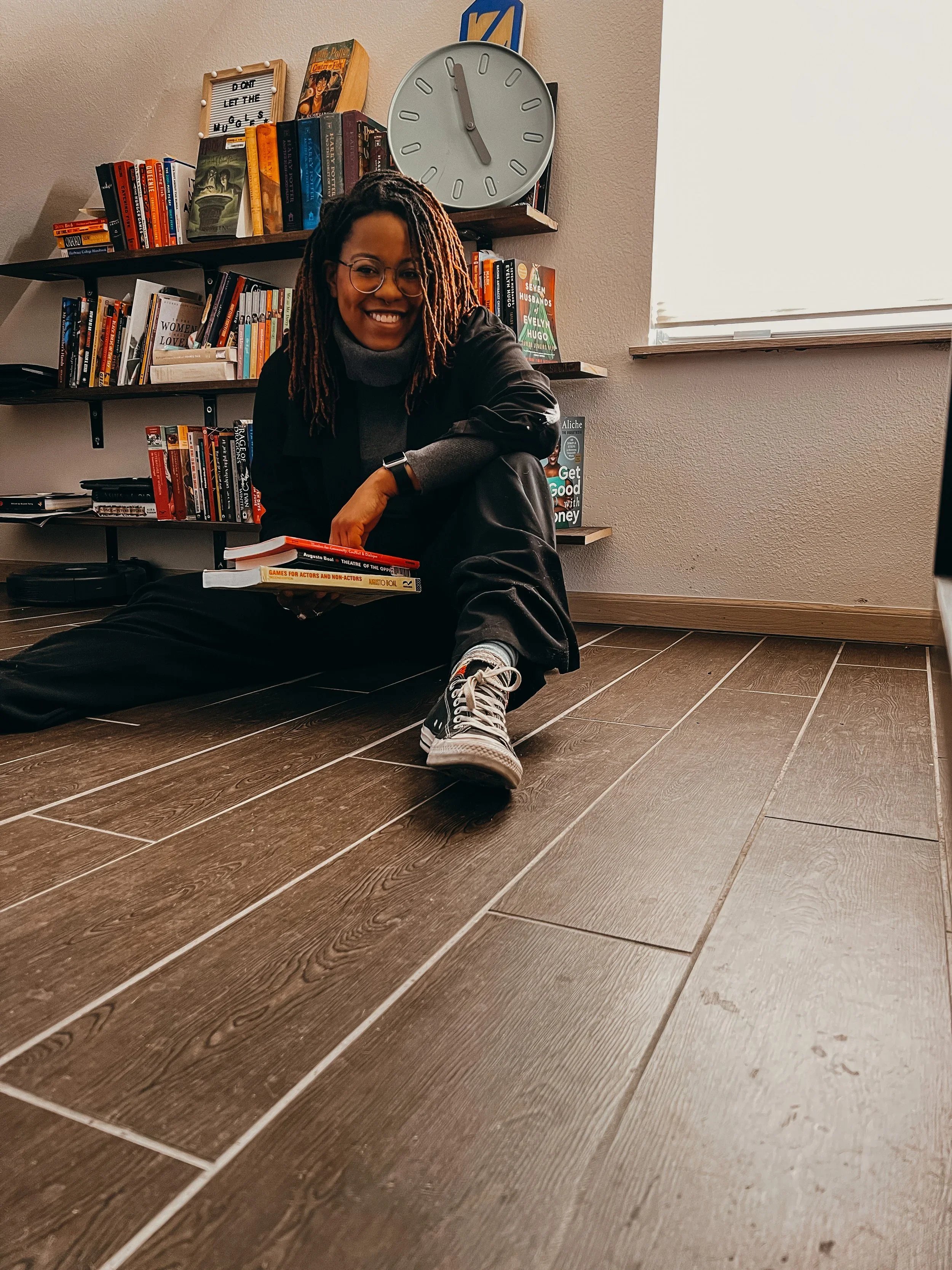 Aryiel sitting in front of a bookshelf holding books, An Aryiel View blog.