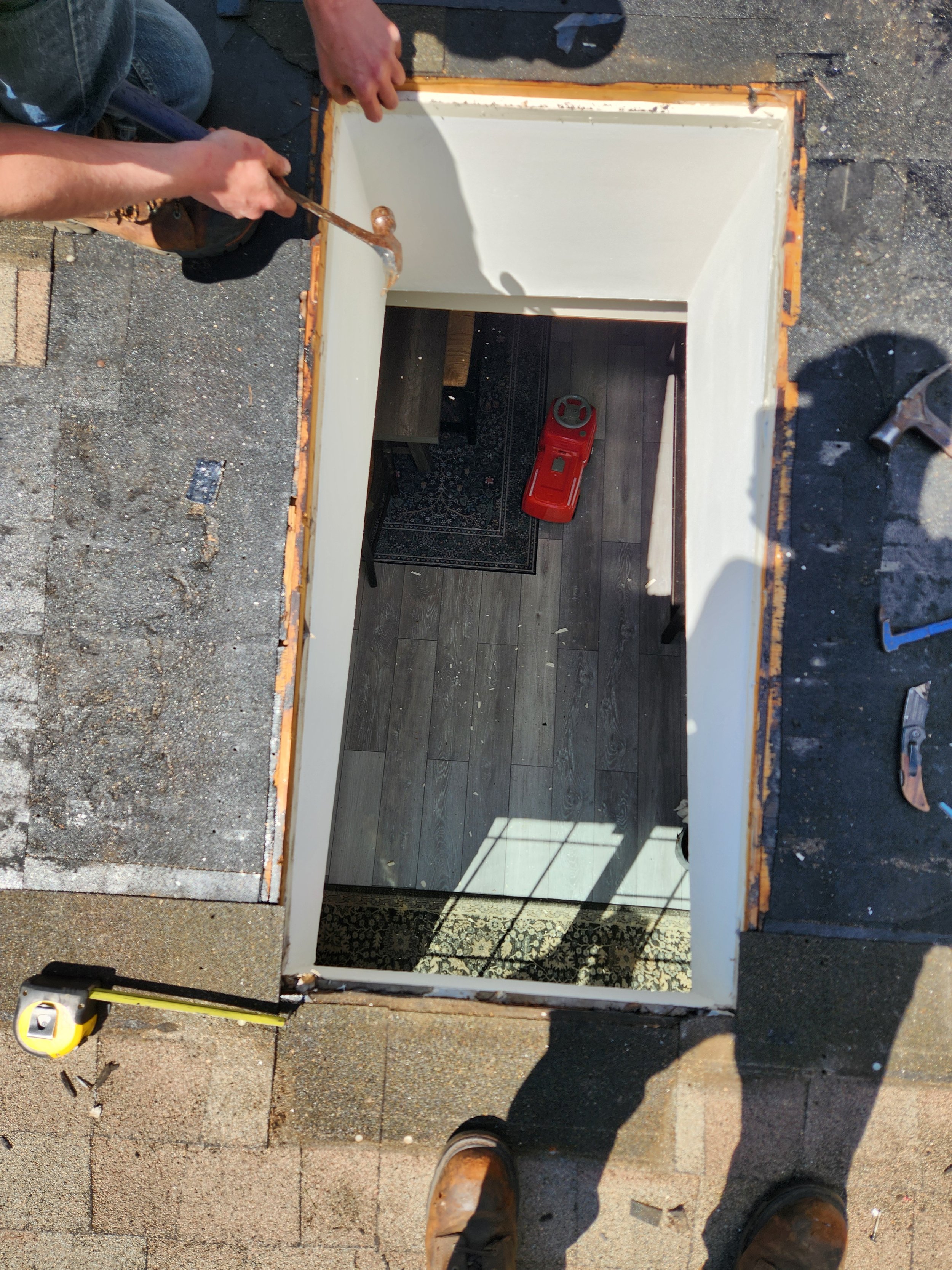 A person is working on the frame of a small doorway or window opening, using a hammer while wearing work boots. The area is outdoors, with construction tools and materials around.