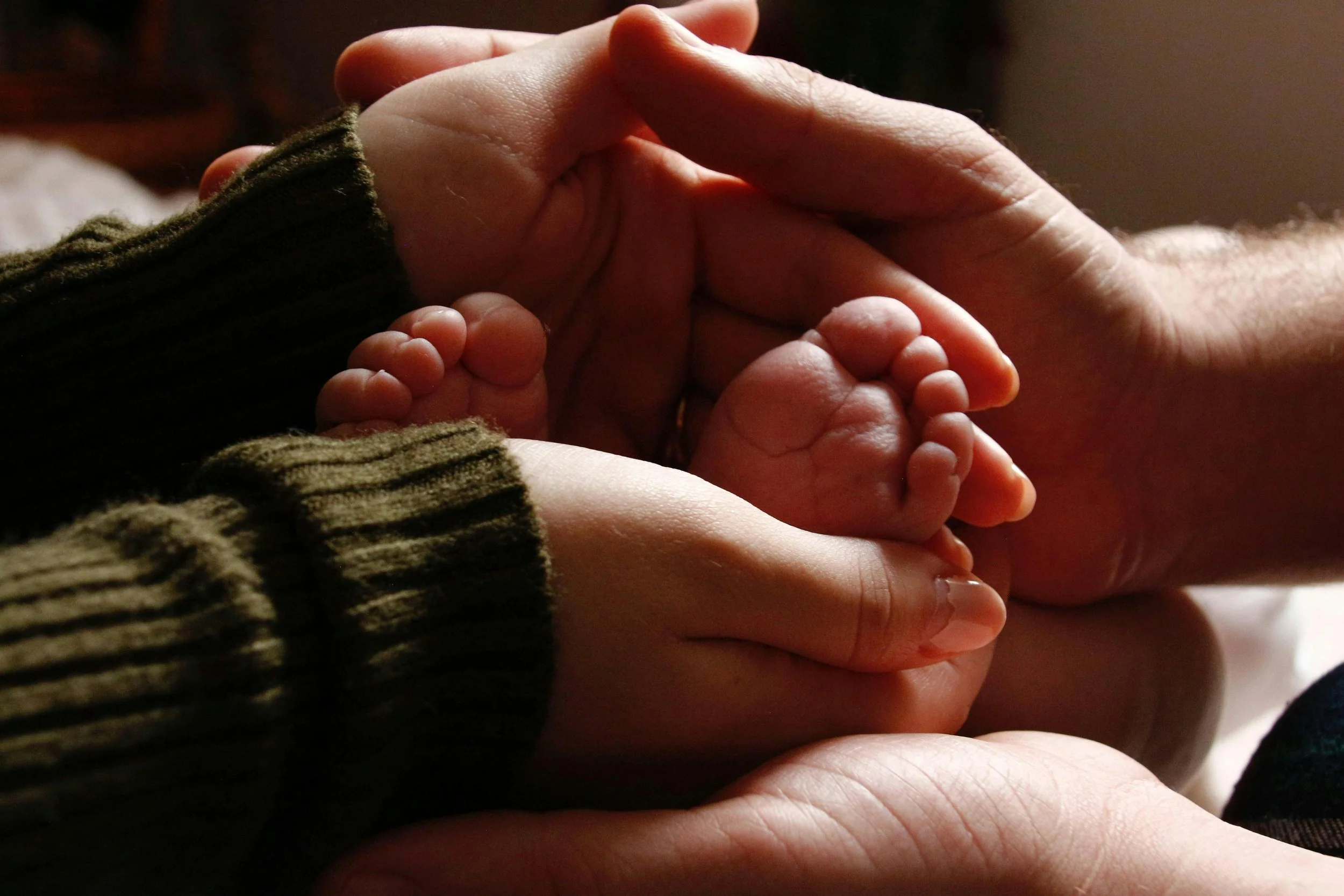 Multiple hands gently holding a baby’s feet.