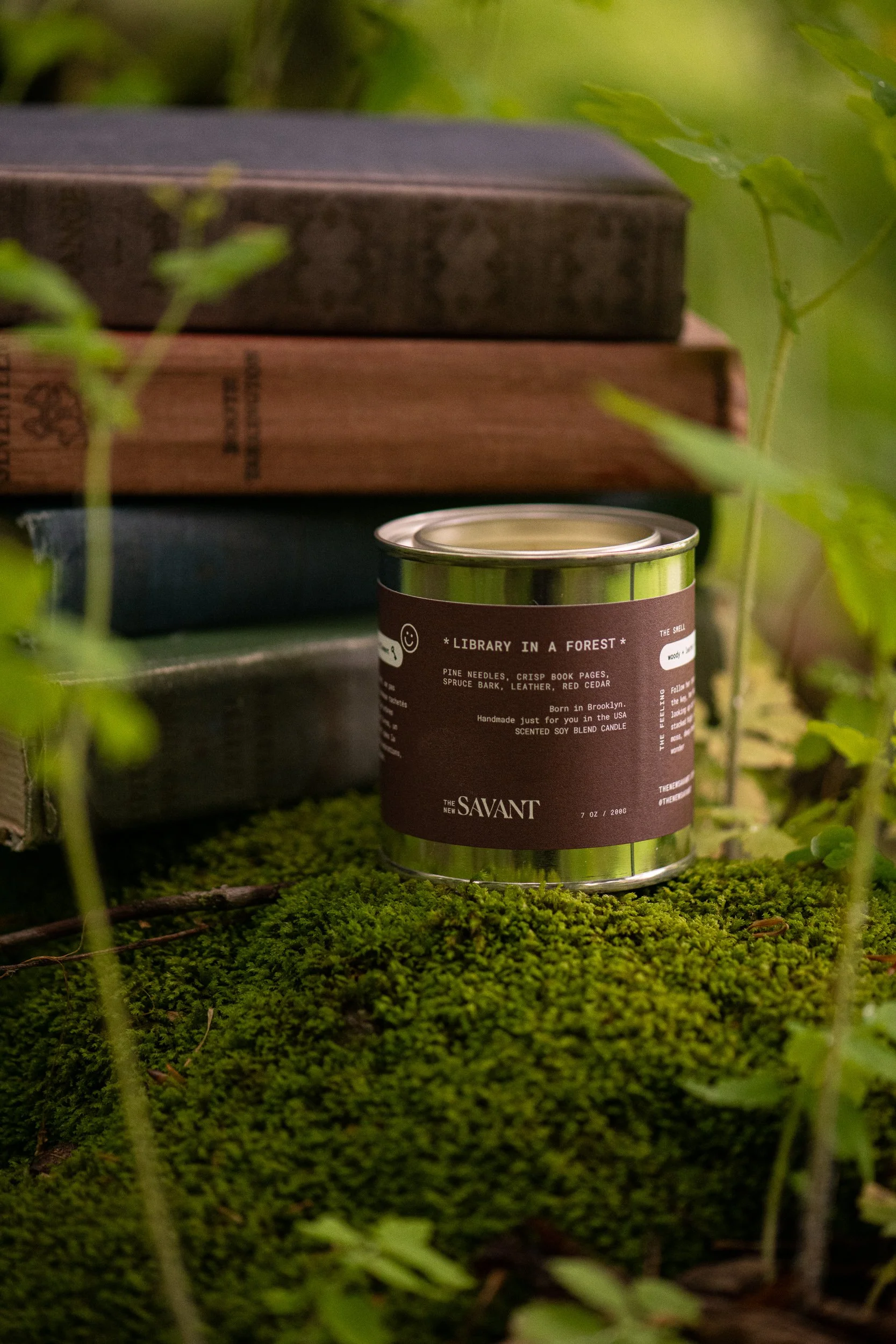 The New Savant Library in a Forest candle displayed on moss beside stacked vintage books in a Vermont forest.