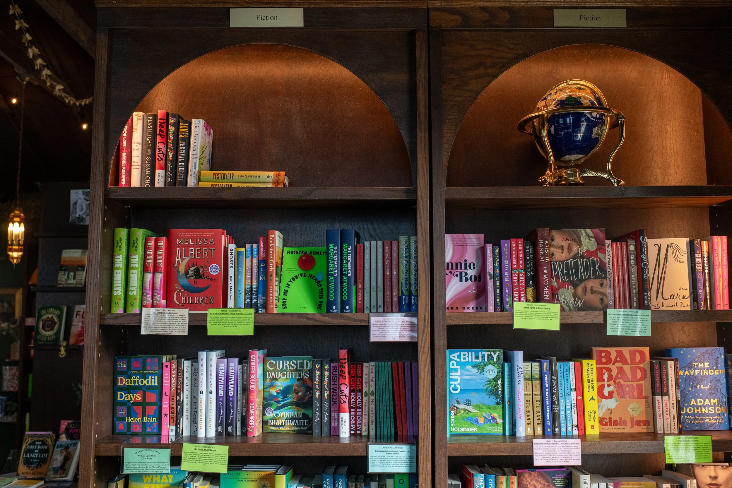 Bookshelf labeled 'Fiction' with various books and a decorative globe with gold accents
