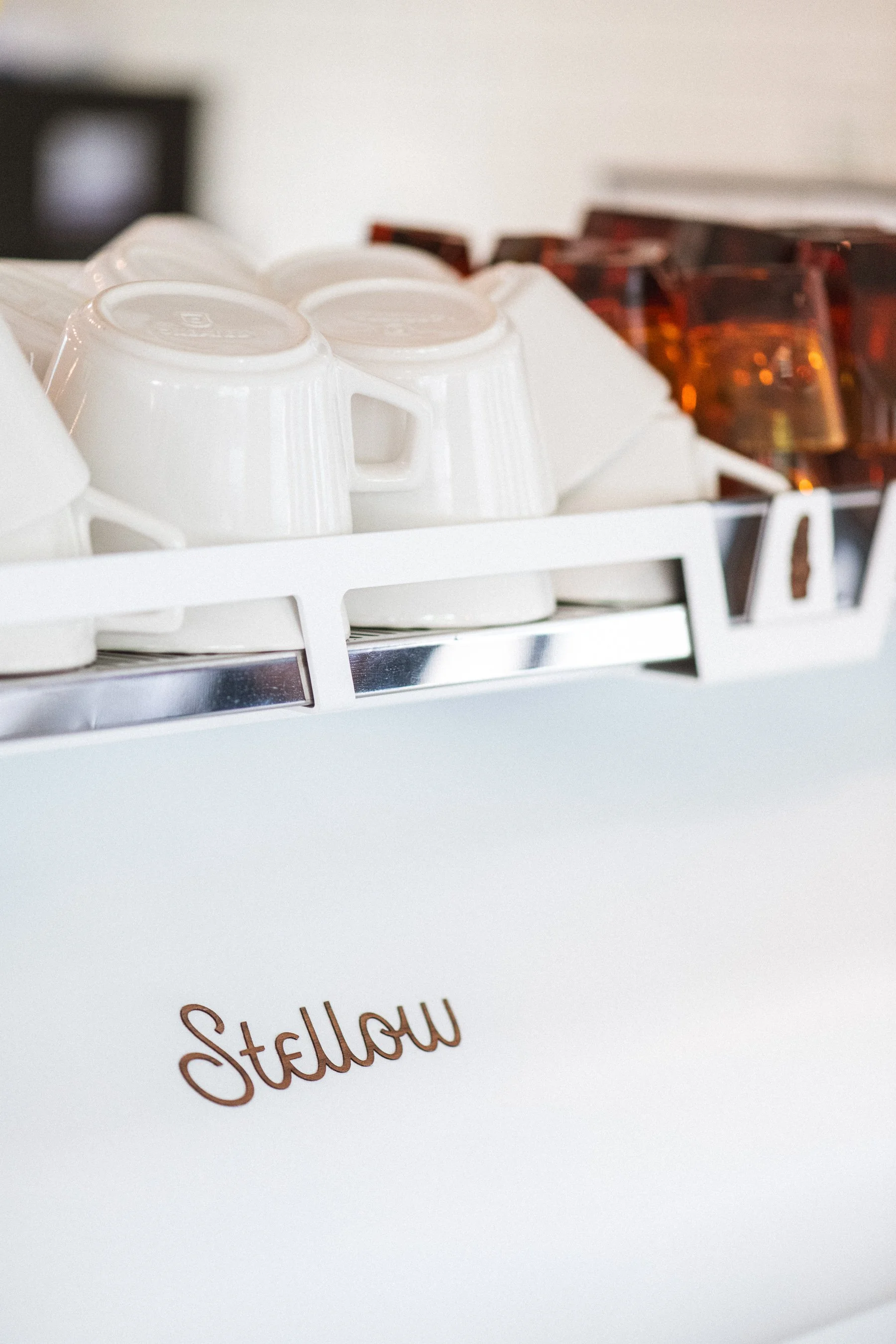 Stacked white coffee cups on a white tray with brown glass cups in the background at Stellow Coffee in Chamblee, GA