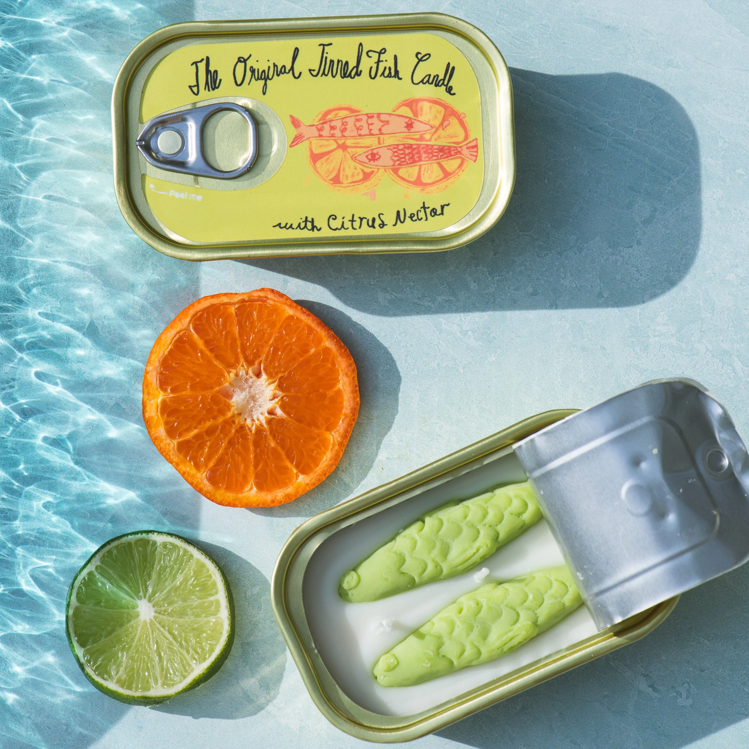 Bright image of citrus and a tinned candle over aqua water rippling below