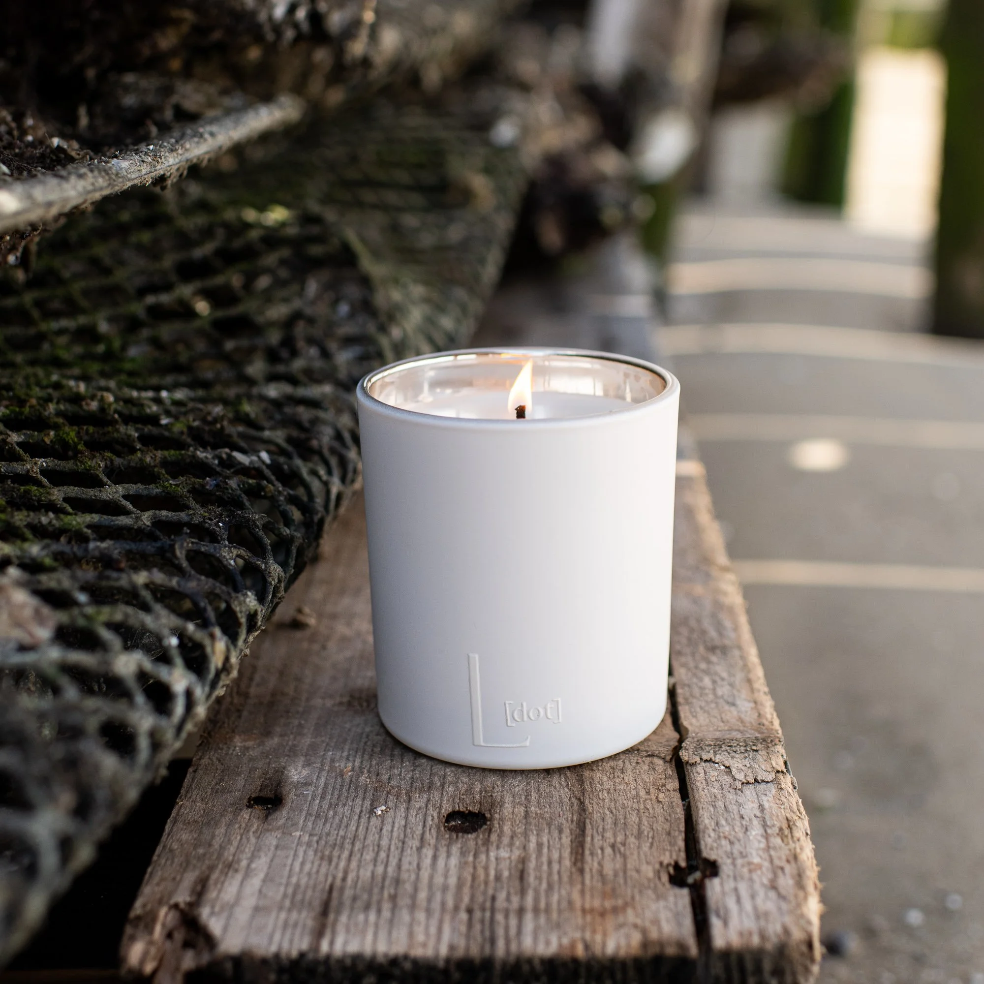 A white candle with a lit flame placed on a weathered dock at the beach.