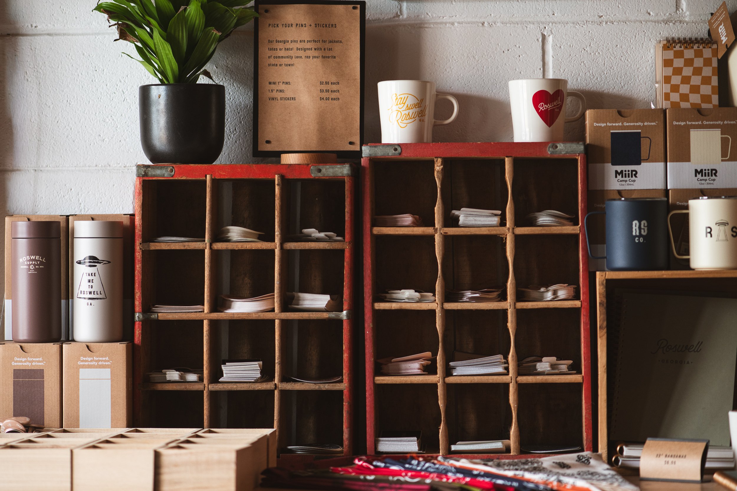 Wooden shelves with stationery supplies, coffee mugs, and a potted plant on a white brick wall.