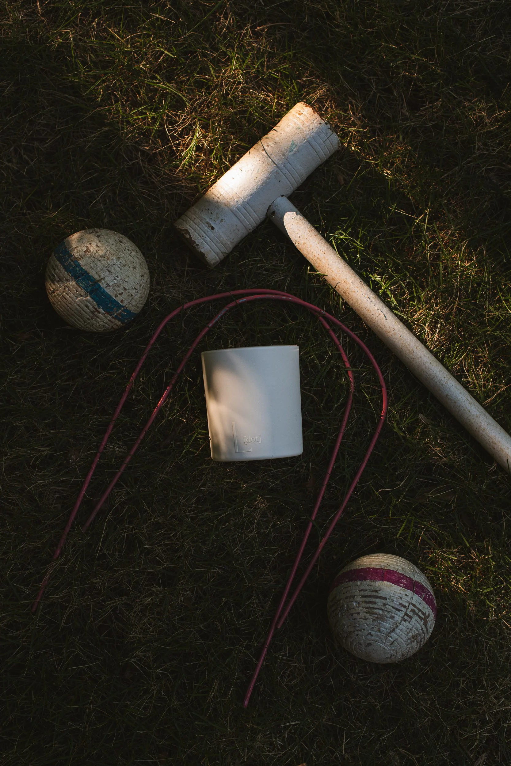 An L Dot Candle is lying amongst an abandoned croquet set.