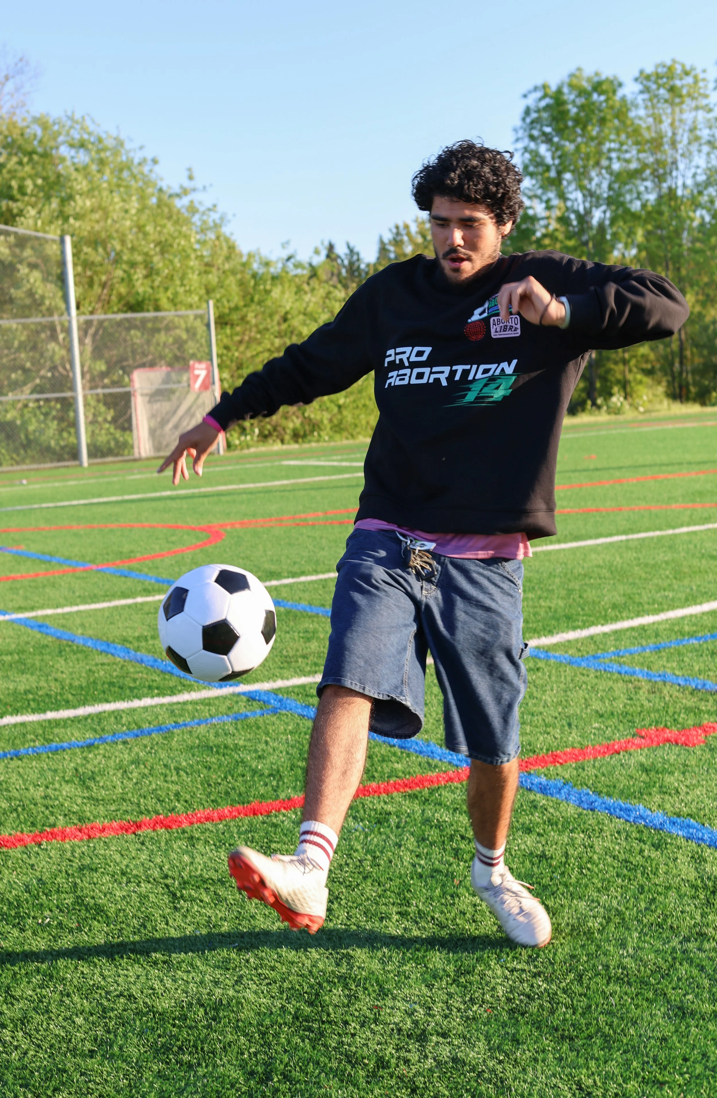 Young man in black sweatshirt kicking a soccer ball on a green field with colorful lines.