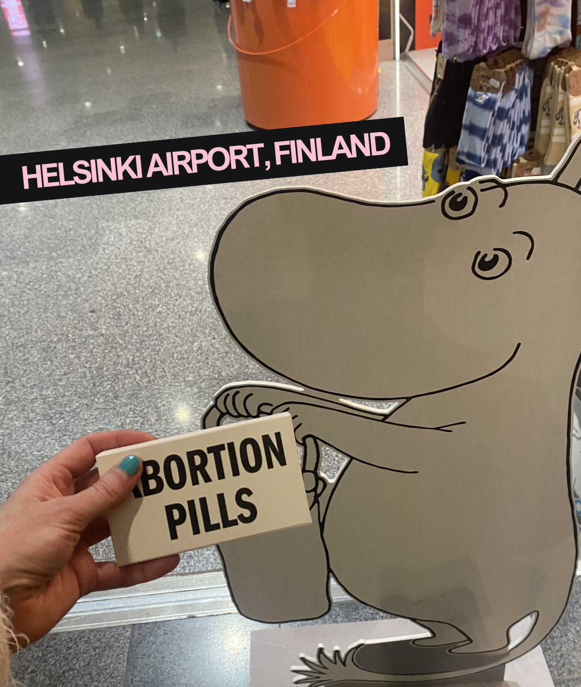 Cartoon character of a kangaroo at Helsinki Airport, Finland, holding a sign that says 'Abortion Pills'; a hand with painted nails is holding a box of abortion pills in front of the kangaroo.