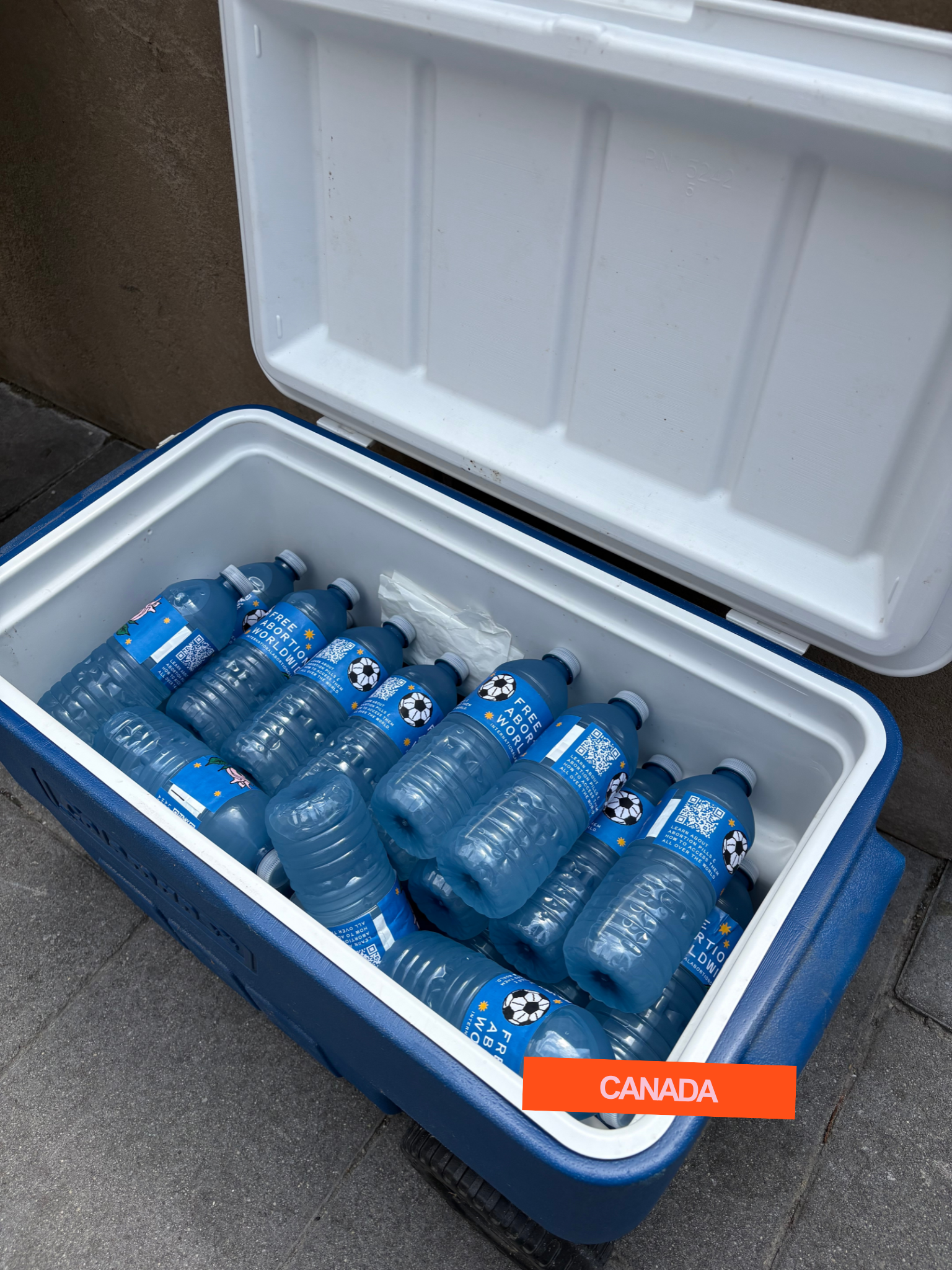 Open cooler with blue bottled water labeled 'Free About the World' with Canadian flag and soccer ball graphic, and a red label indicating 'Canada'.