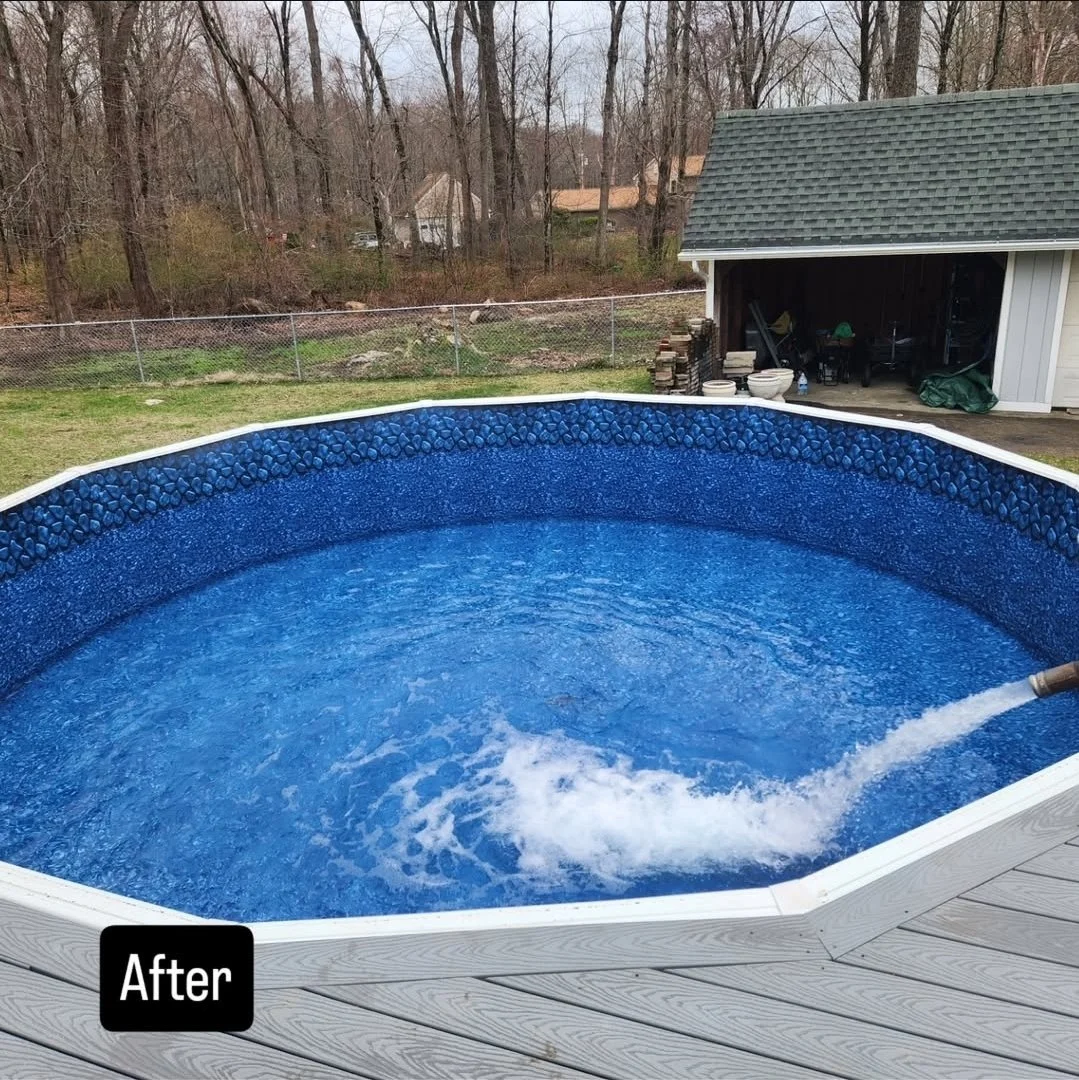 An above-ground swimming pool with blue interior walls and a deck, filled with water, located in a backyard with trees and a shed in the background.